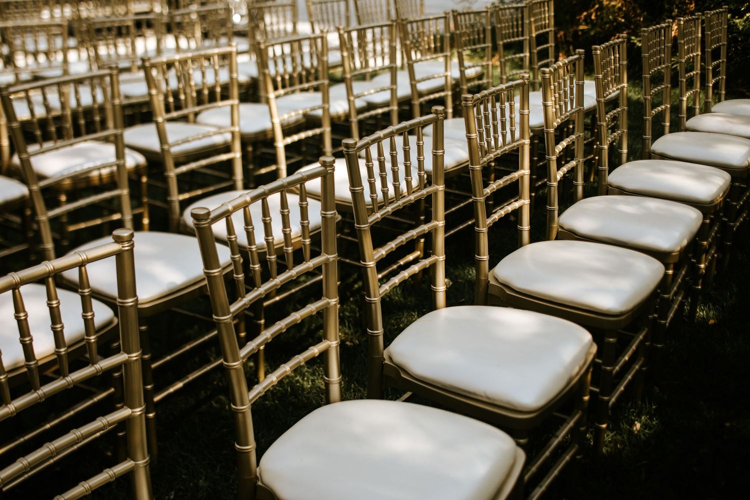 Row of gold chiavari chairs with white cushions at wedding ceremony setup.