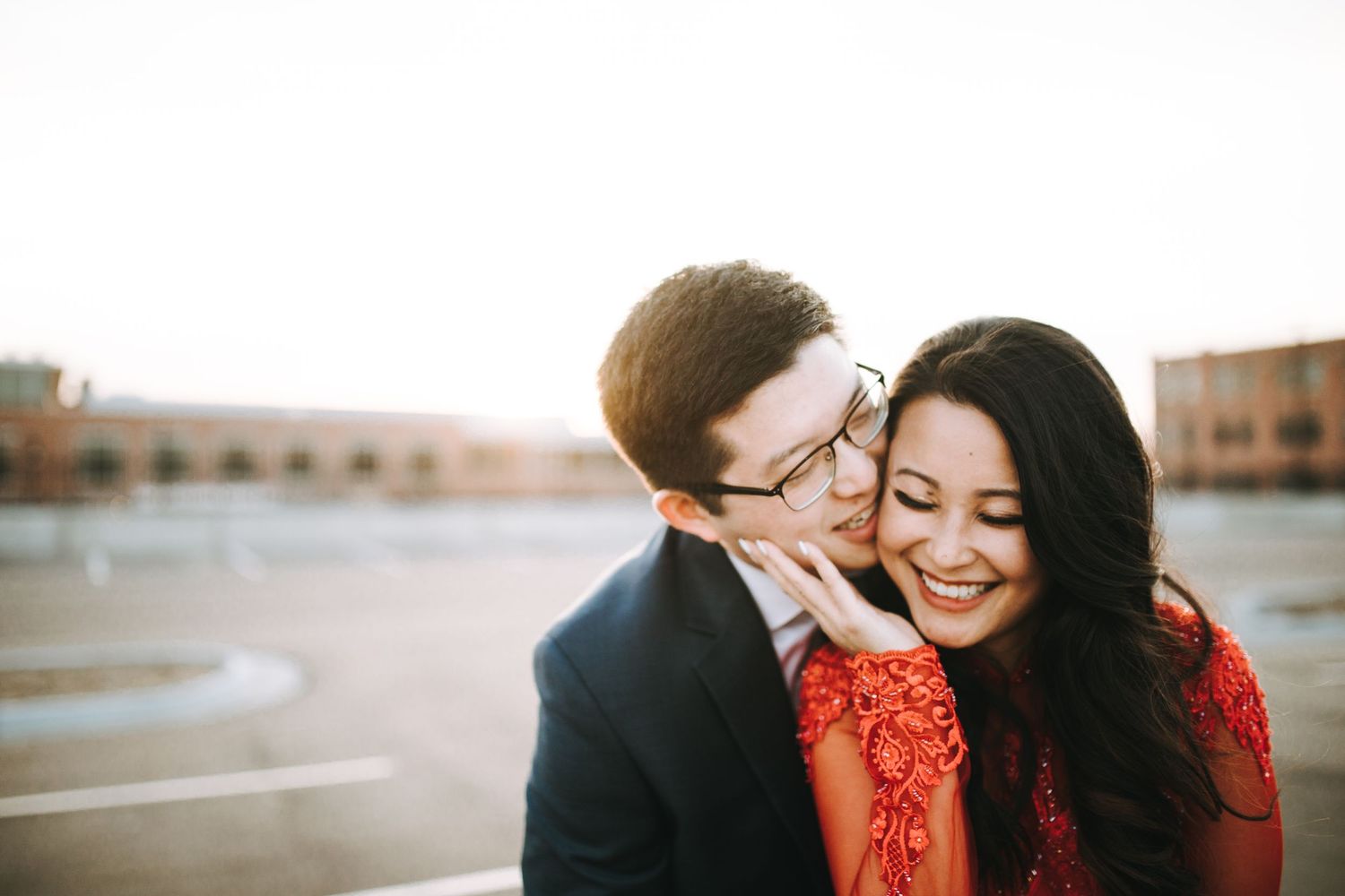 Romantic couple in formal attire embracing and laughing together during an outdoor photo session at sunset.
