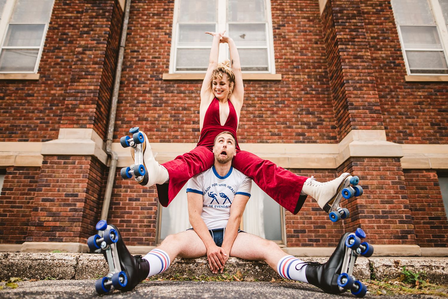 Playful poses against red brick building wall in casual attire.