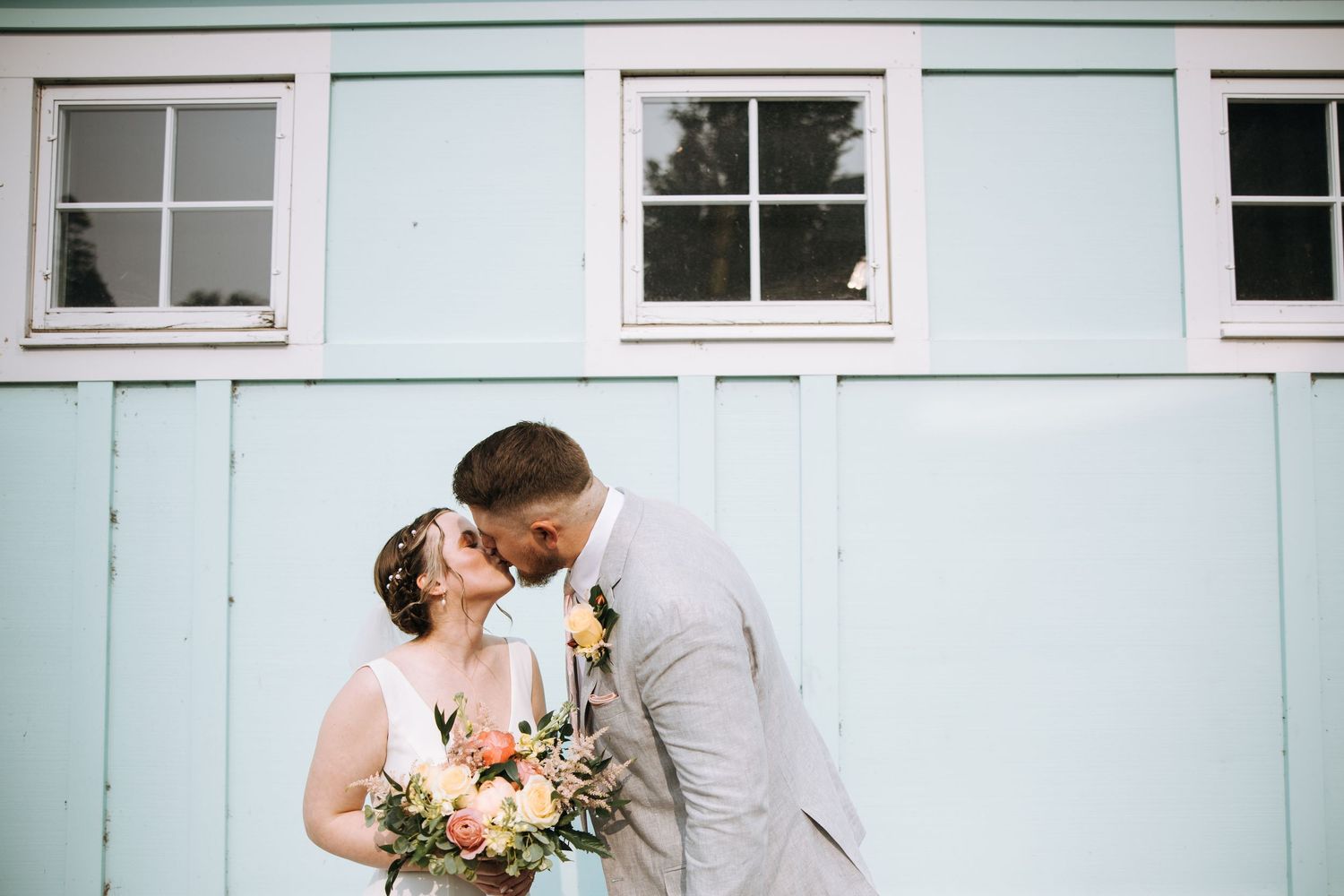 A couple embraces in front of a light blue building with white trim and windows.