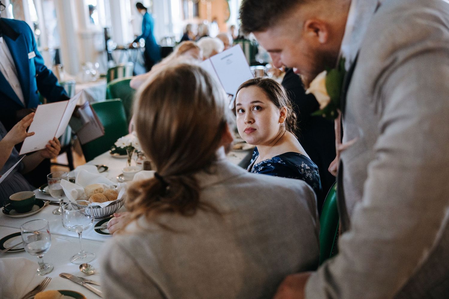 Wedding guests enjoying a meal at elegant reception tables in a bright, airy venue.