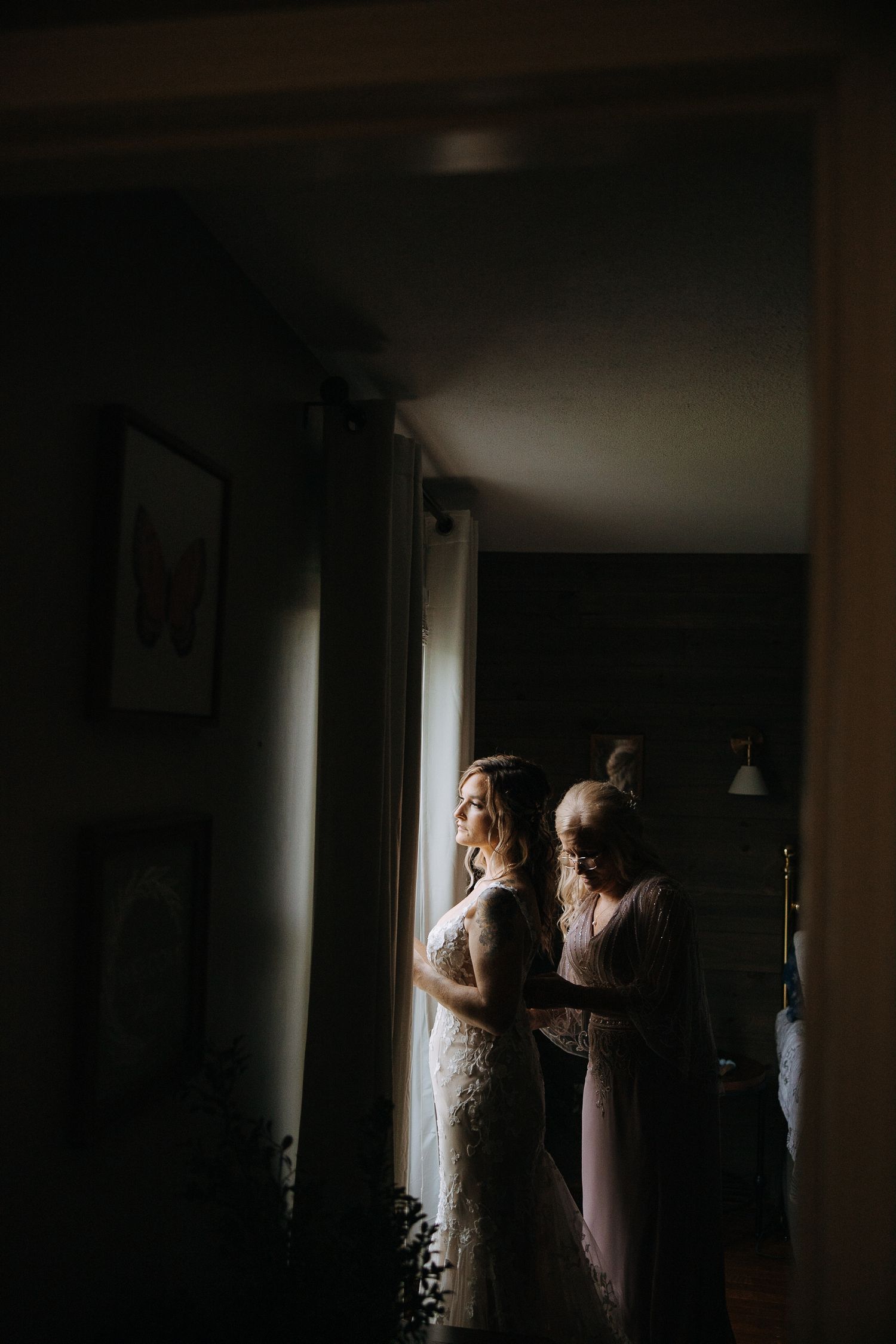 Dramatic silhouette of wedding preparations in dark moody room with window light.