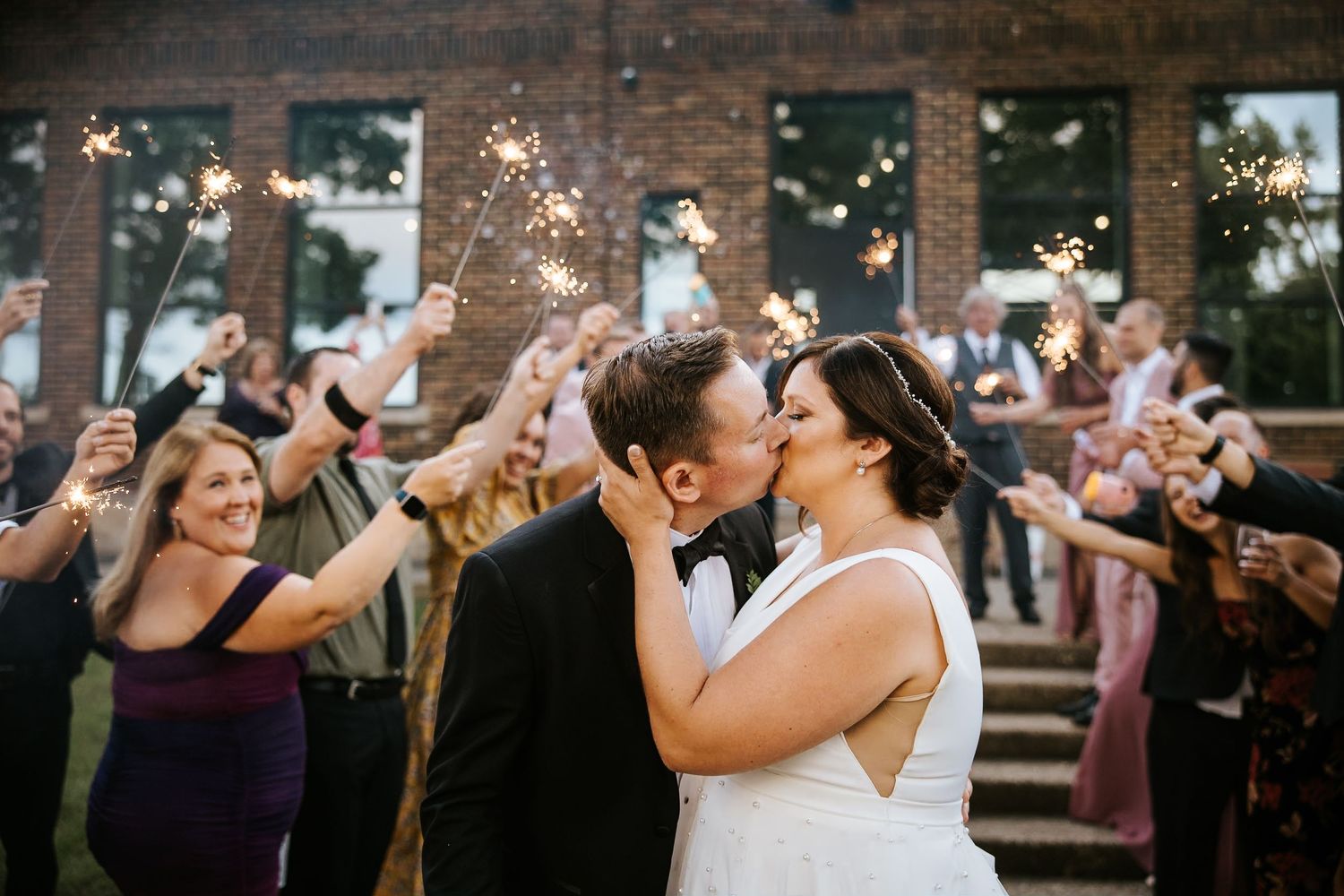 Wedding celebration with guests throwing confetti outside brick building at sunset.