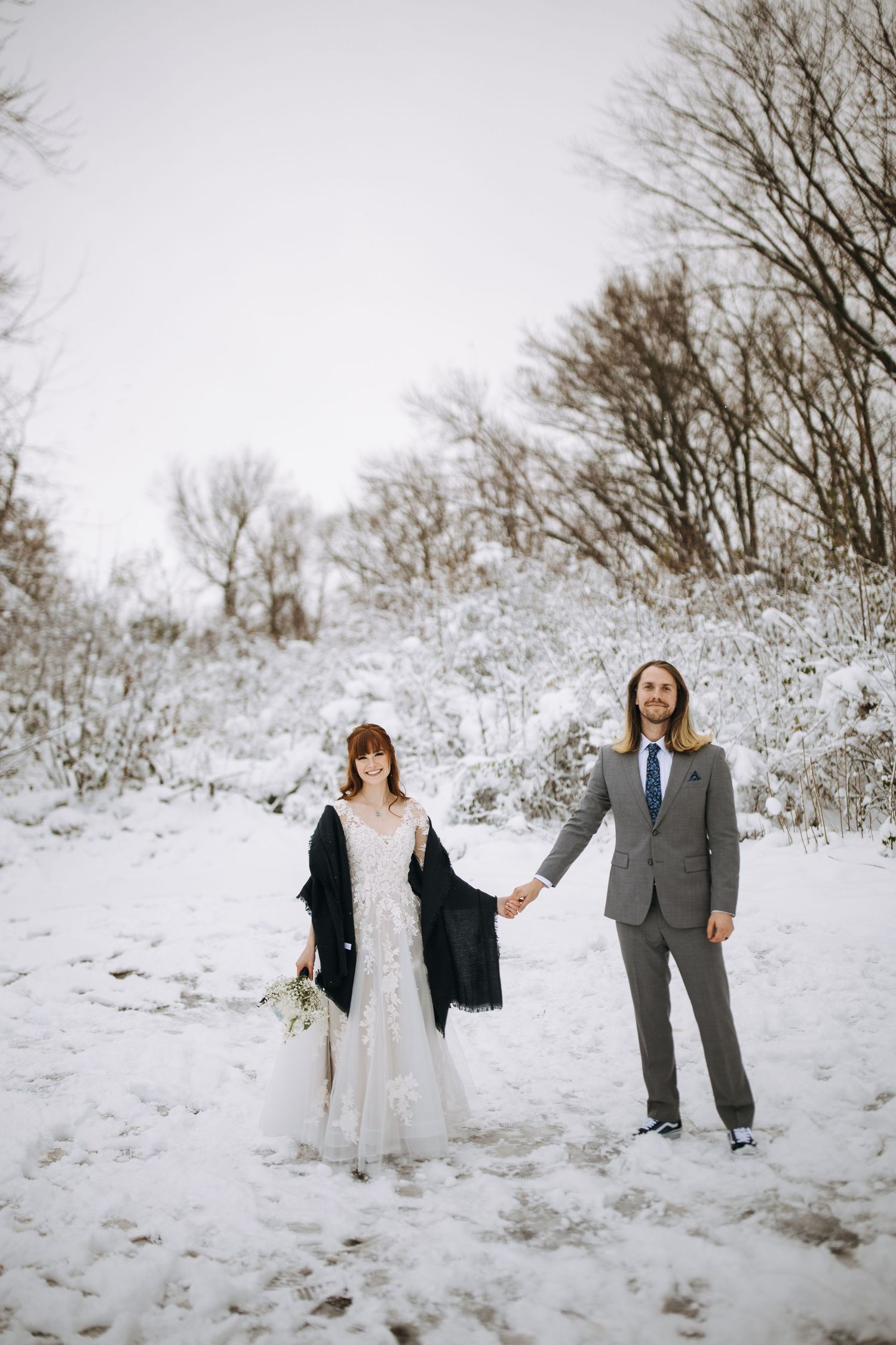Wedding party playfully posing in a snowy winter landscape with bare trees in the background.