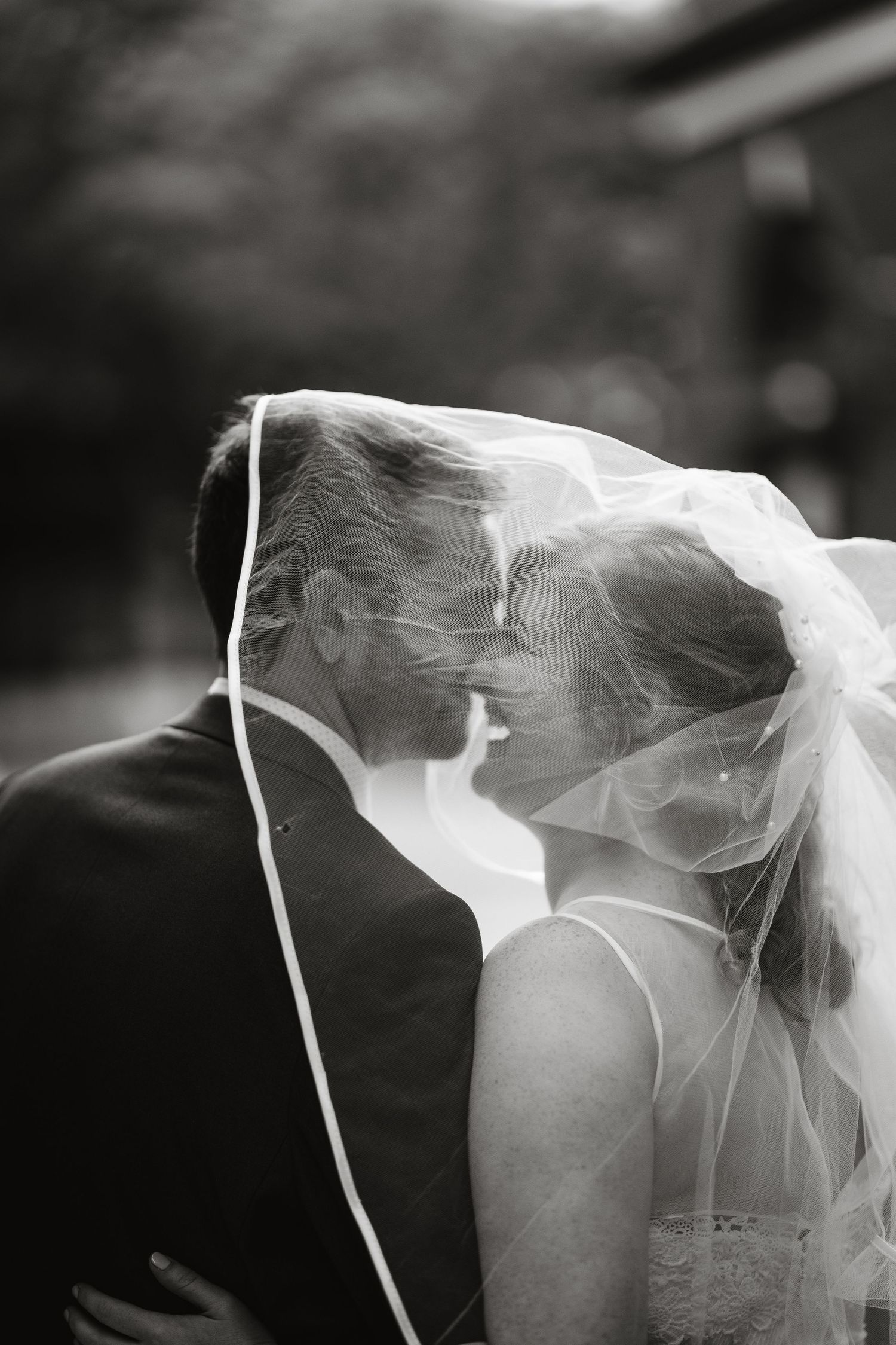 A romantic black and white portrait of newlyweds under a flowing veil.