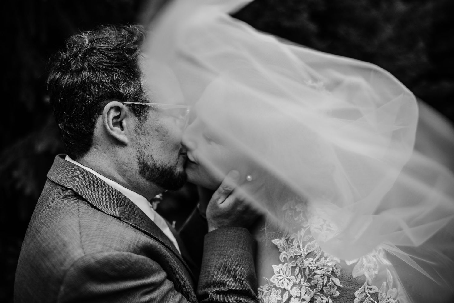 Intimate black and white moment shared under flowing white veil.