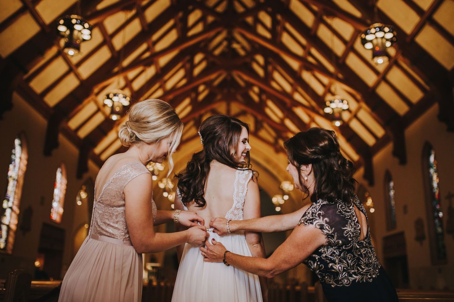 Wedding party joins hands in a circle during a reception in a rustic wooden barn venue with exposed beams.