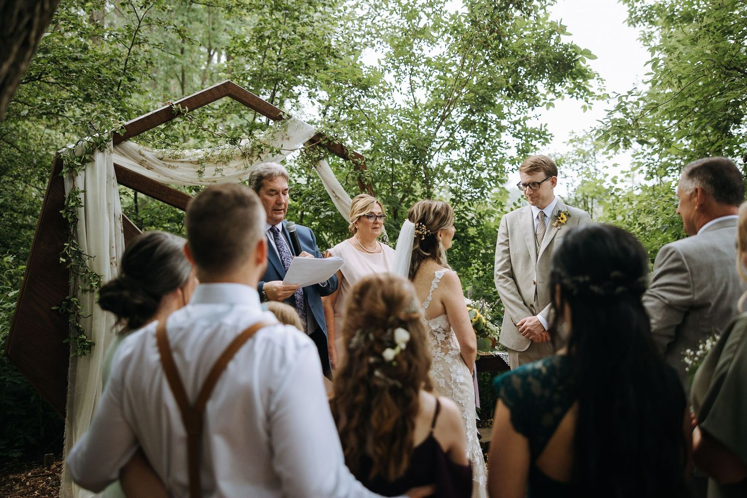 Wedding celebration with guests gathered under trees during an outdoor ceremony.