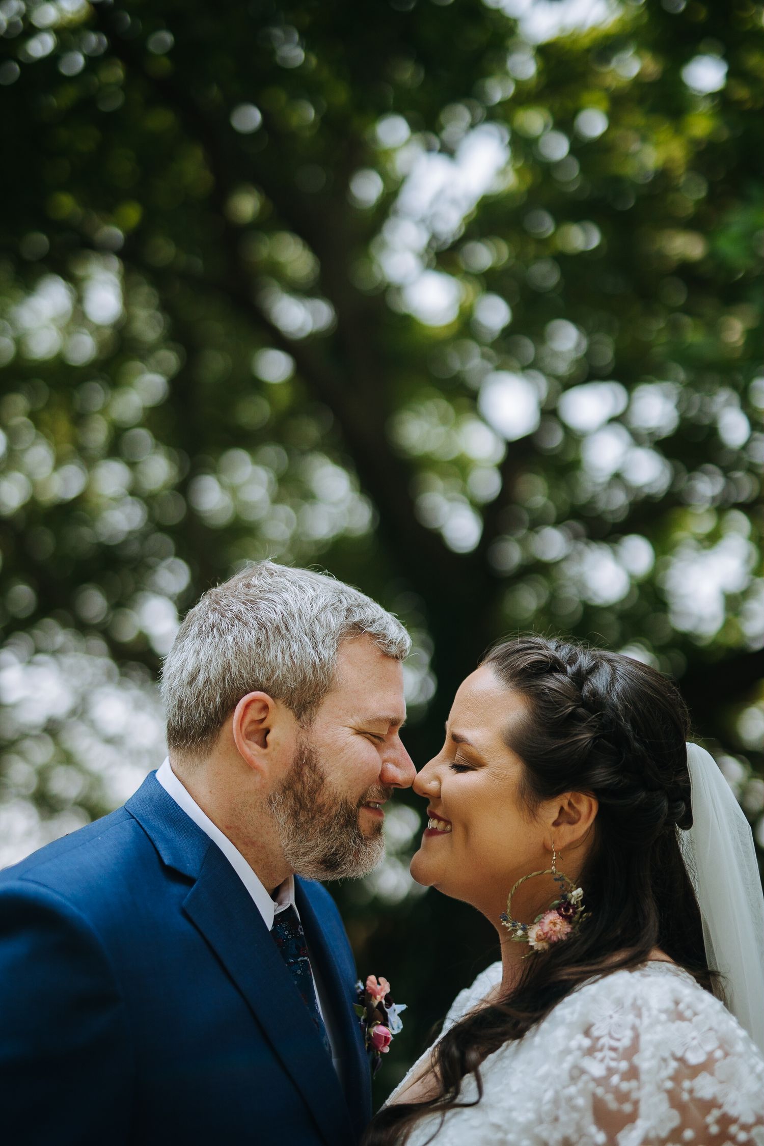 Intimate wedding moment captured under green leafy trees in natural lighting.