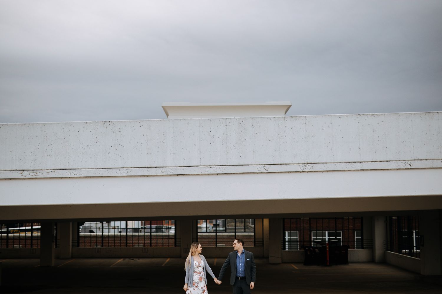A wedding couple stands beneath a modern white architectural structure on an overcast day.