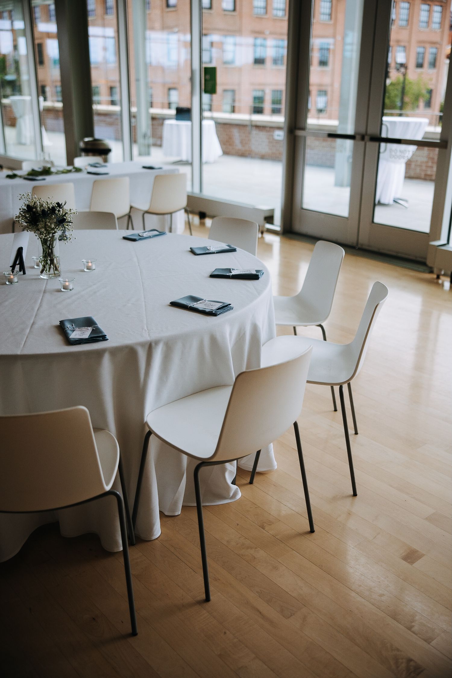Modern reception venue with white round tables and chairs set up on light wooden floors.