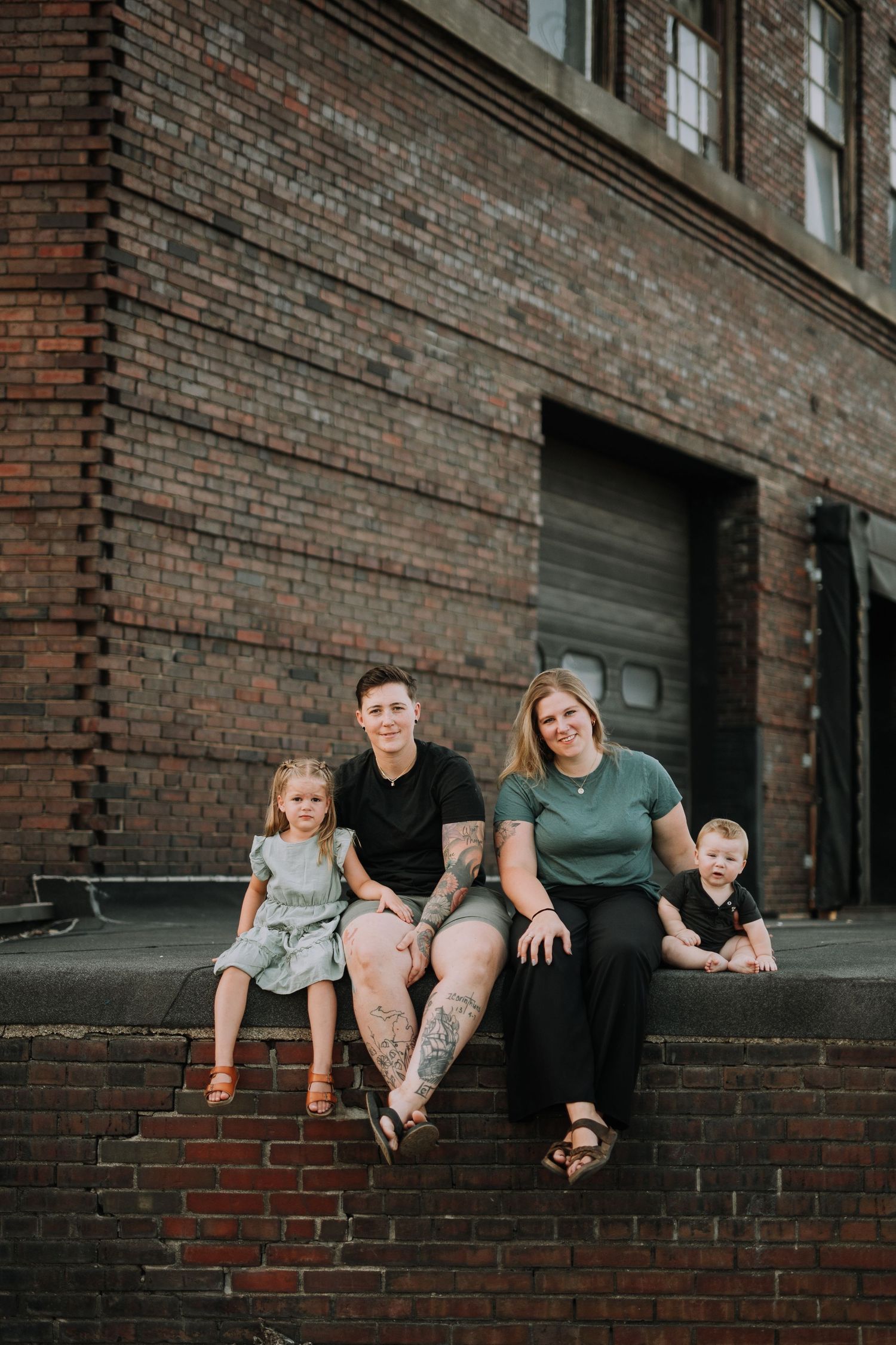 Family sitting together on brick ledge outside building in casual portrait.