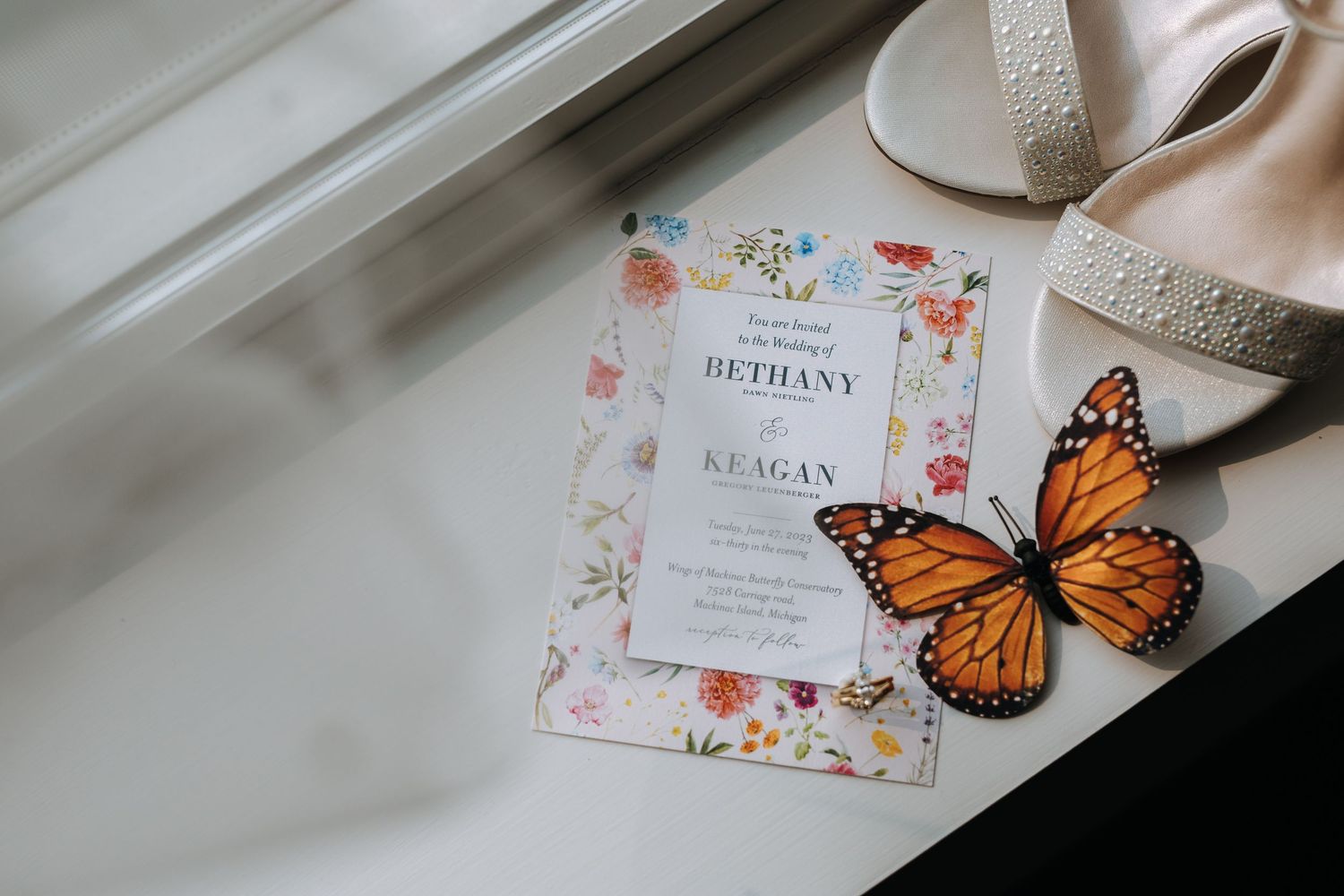 Wedding invitation with floral design and decorative monarch butterfly on white surface.