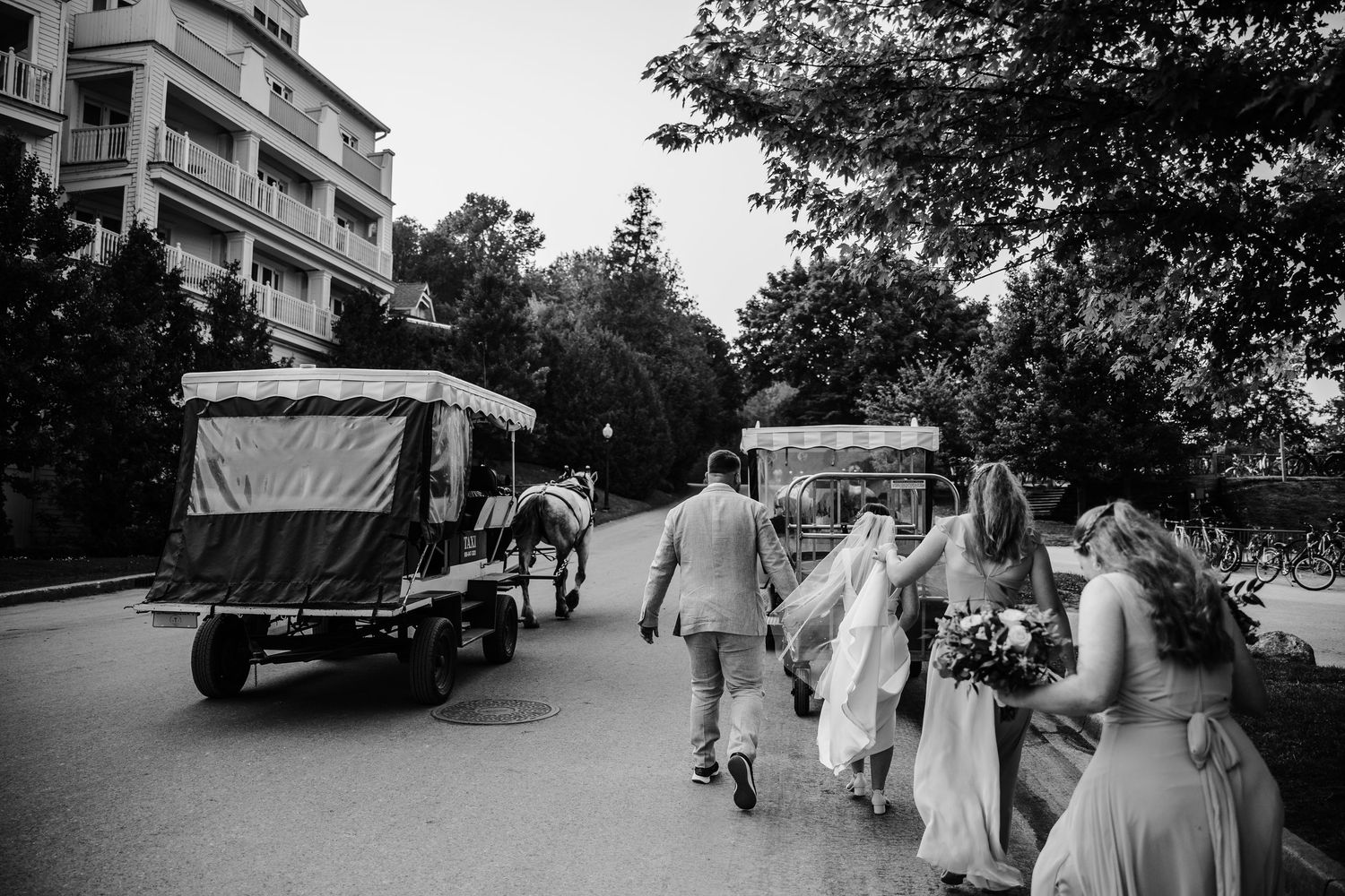 Black and white photo of a tree-lined path with people walking during a wedding ceremony.