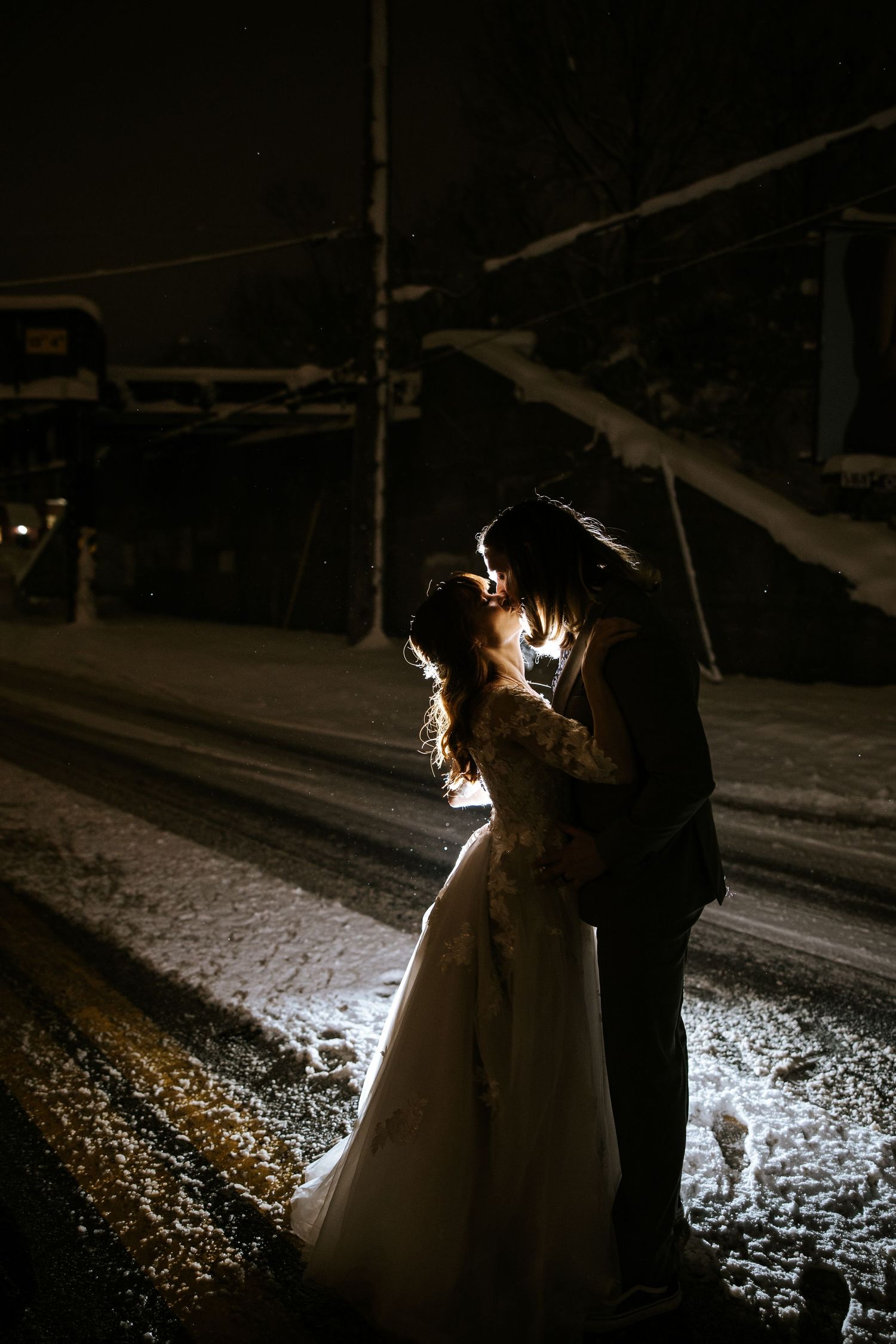 Dramatic nighttime portrait of couple in snow with backlit silhouette.