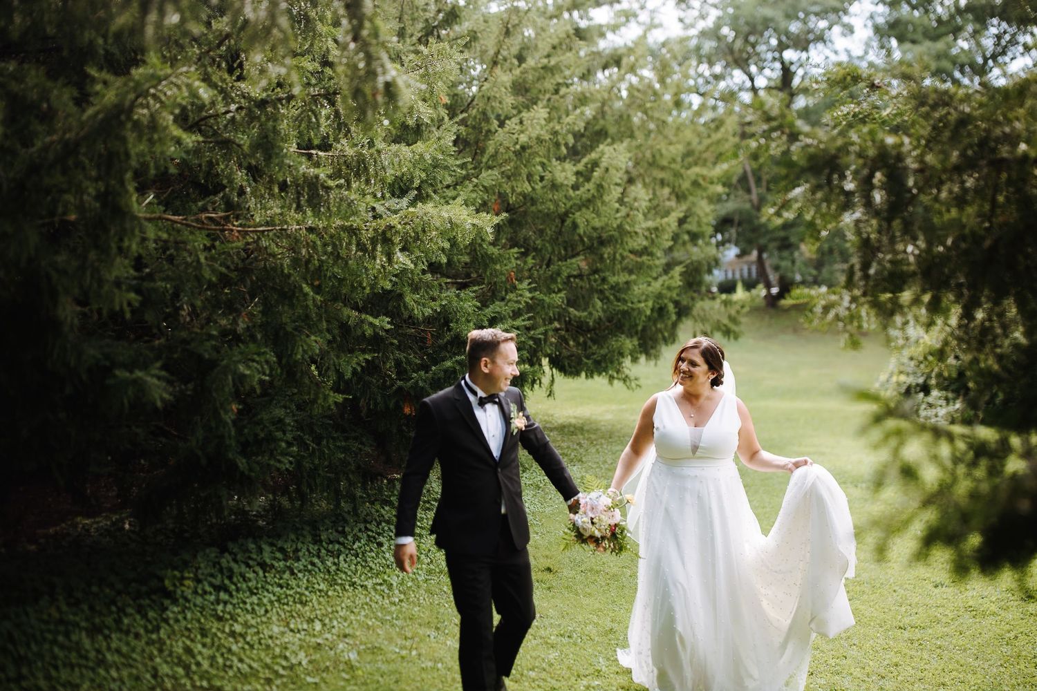 Wedding couple walks together on a lush green path surrounded by trees on their special day.