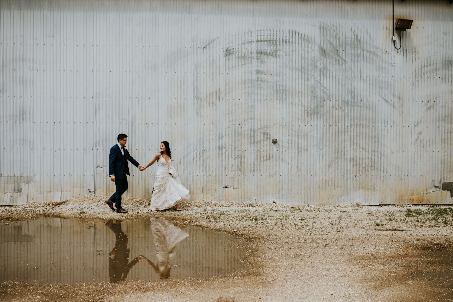 Wedding couple and guests arranged in a line against a rustic white wall for creative group photos.