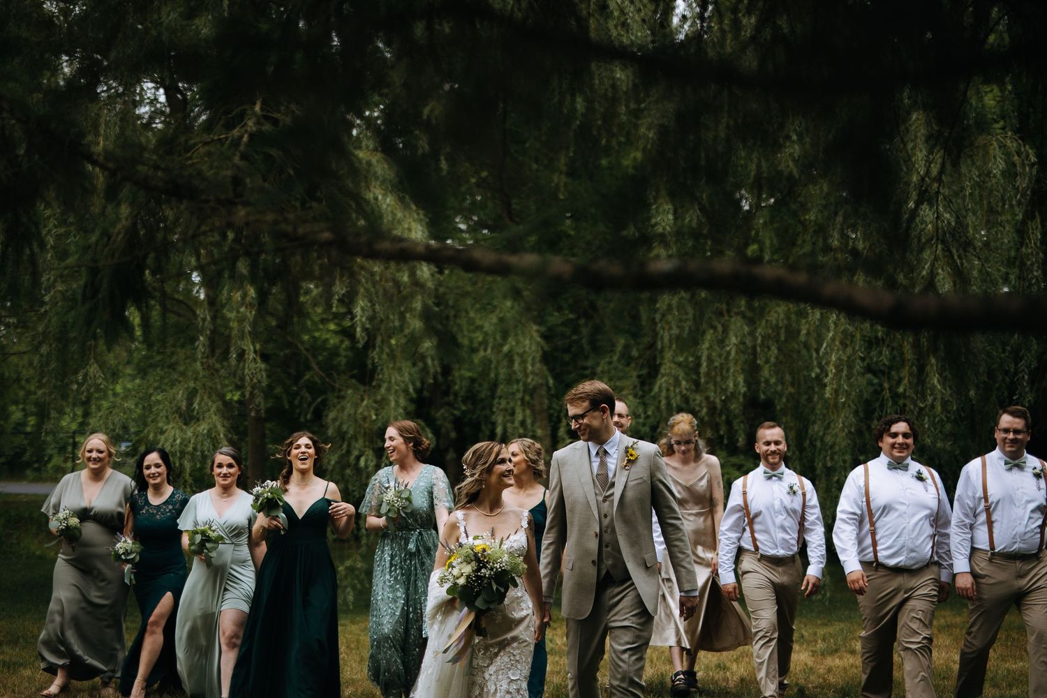Wedding party members walking together outdoors through a lush green garden setting.