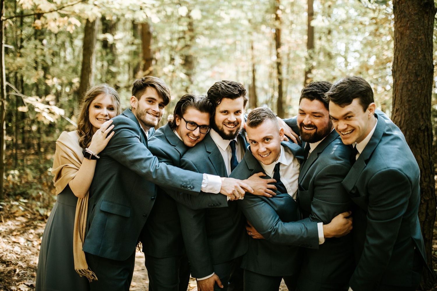 Groomsmen share a playful moment in a wooded setting during wedding photos.