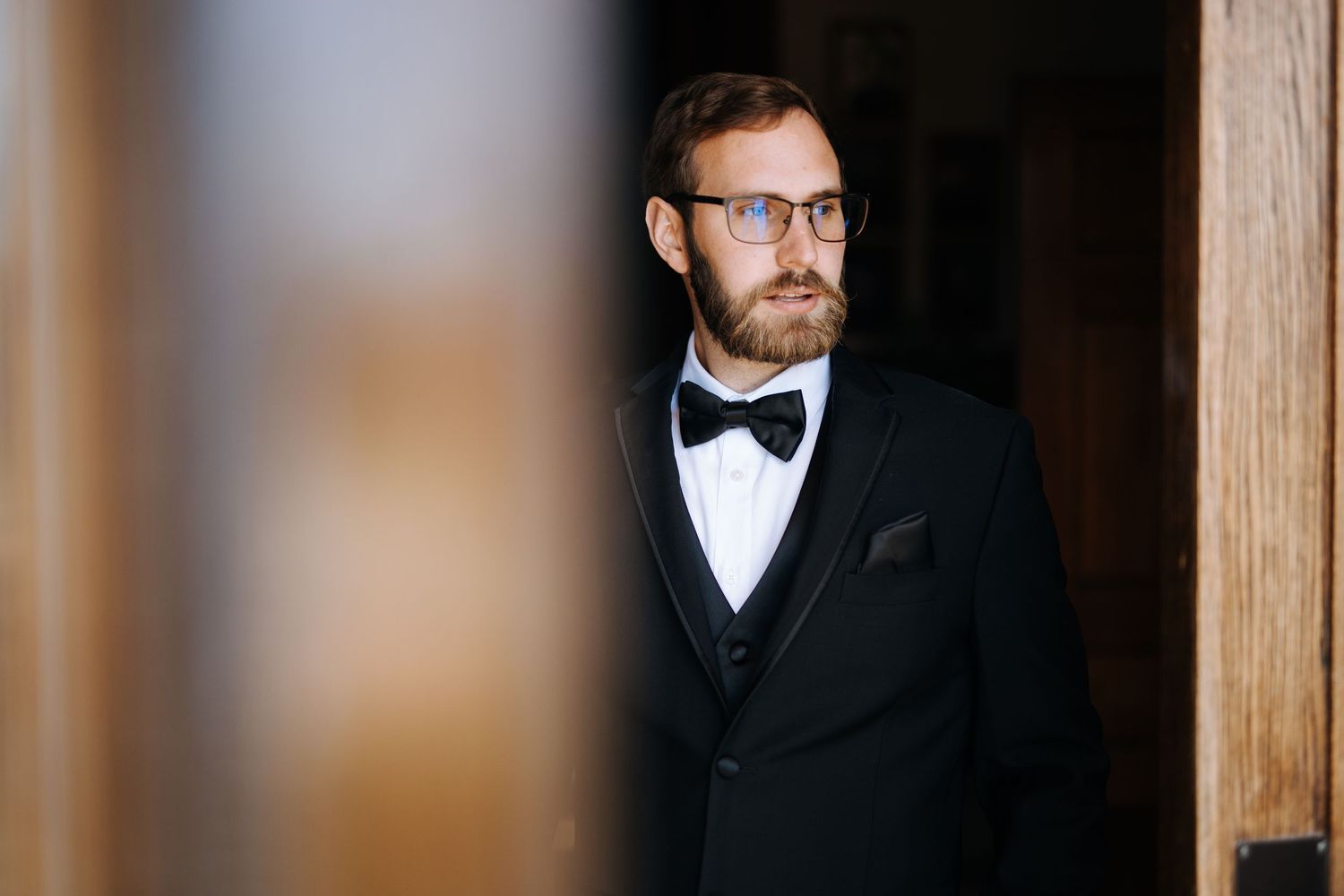 Classic groom portrait showing formal attire details against wooden backdrop.