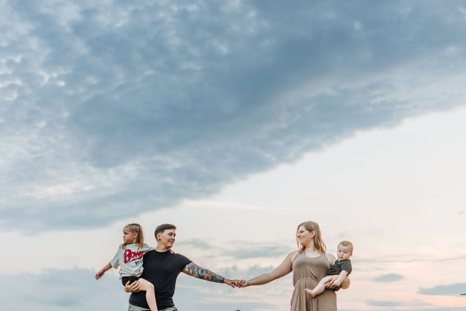 Couple holding hands against cloudy sky during sunset.
