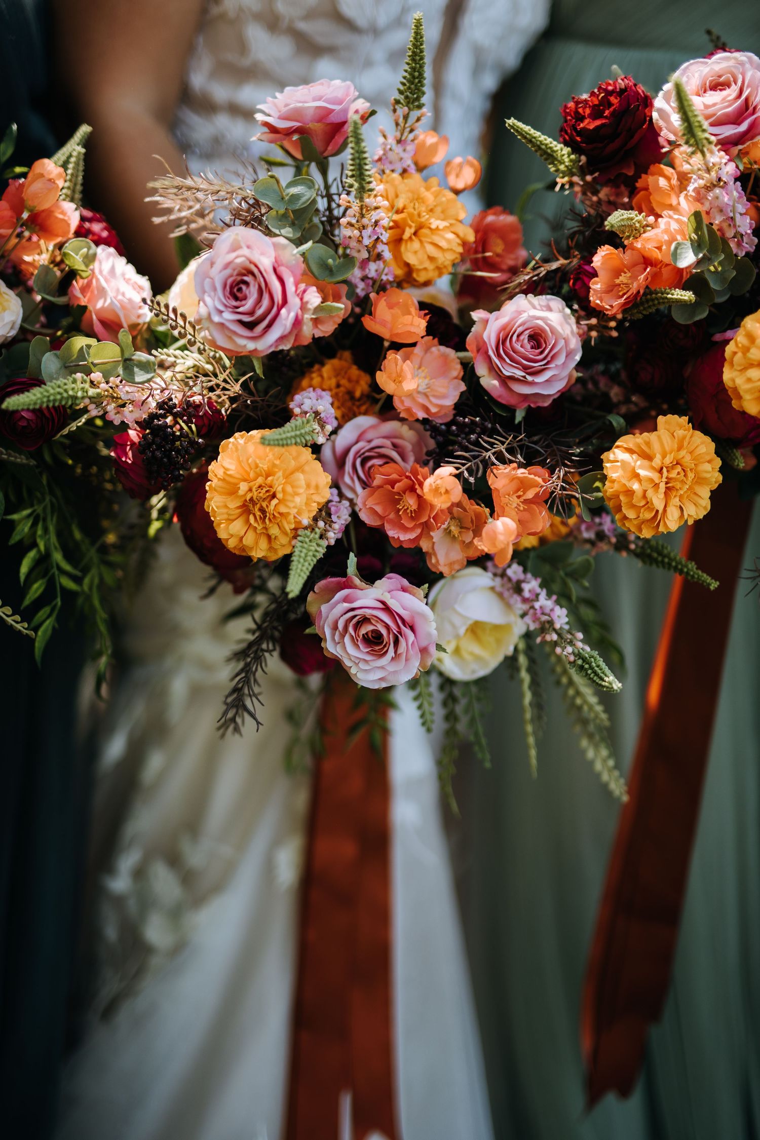 Vibrant wedding bouquet featuring pink roses, orange flowers, and greenery.