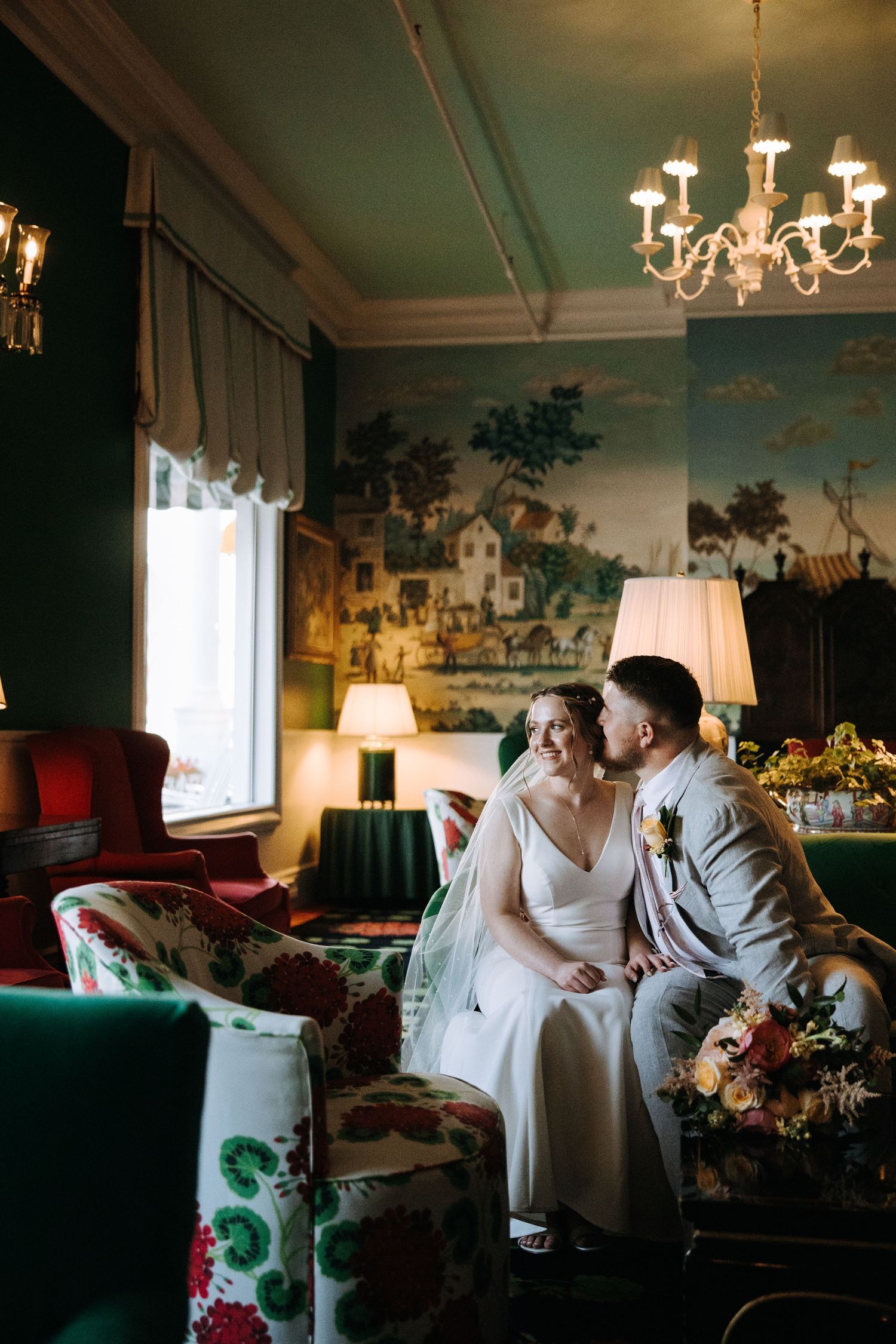 Intimate moment in luxurious room with vintage wallpaper and chandelier lighting.