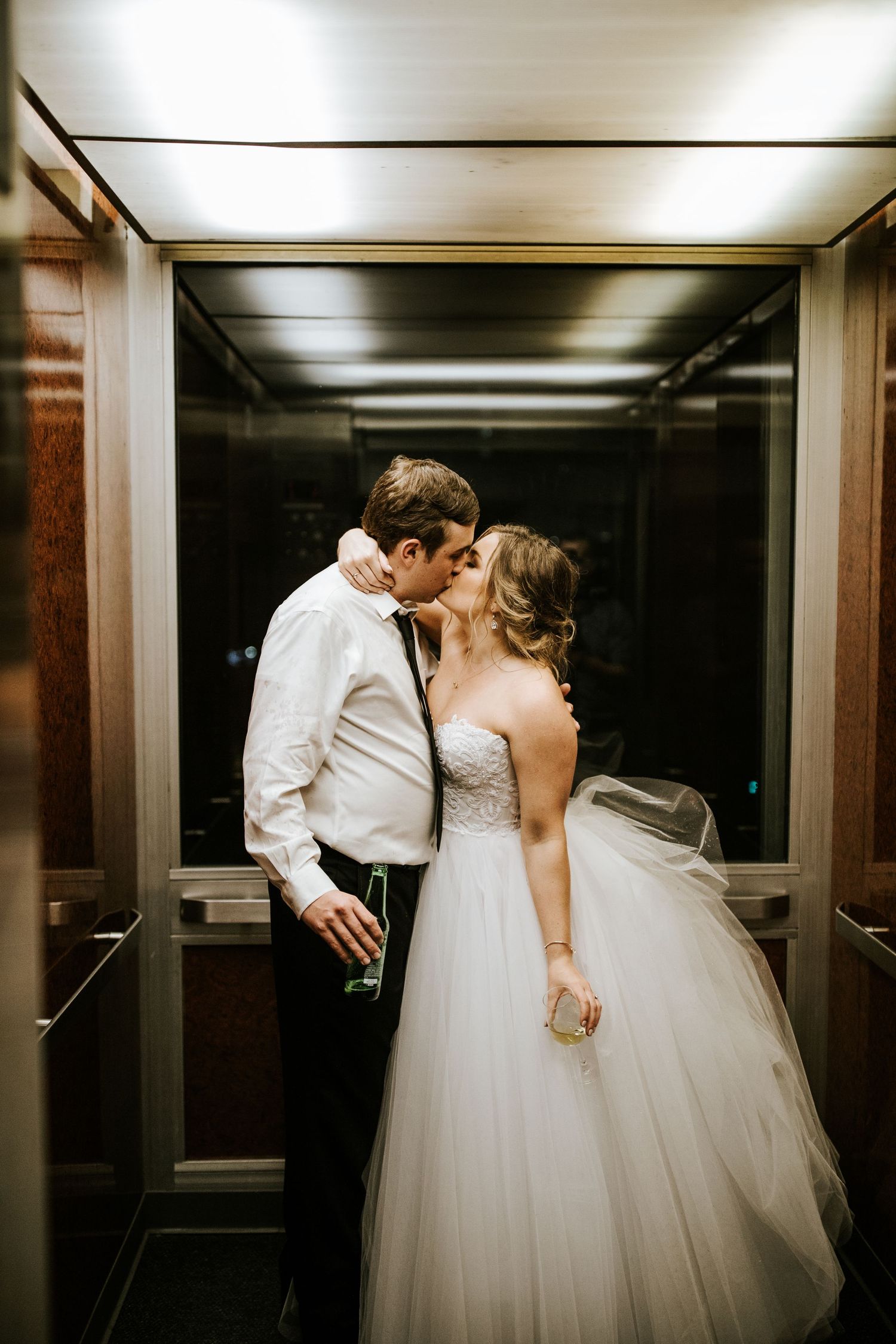 A romantic moment captured in an elevator between newlyweds in formal wedding attire.