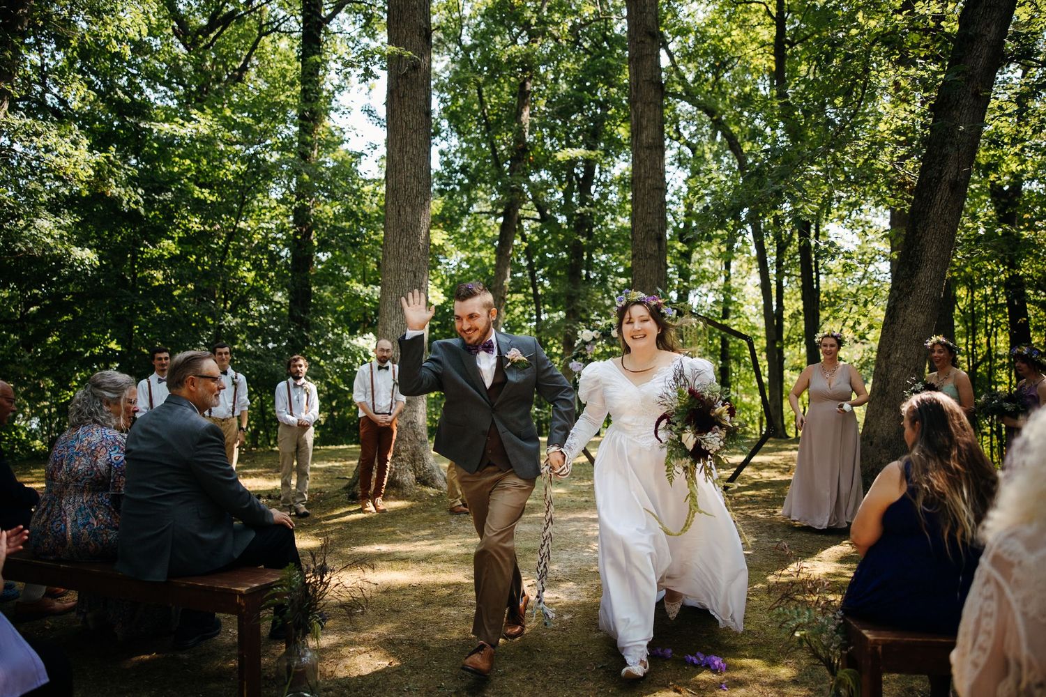 Wedding guests gathered in a shaded woodland setting for an outdoor ceremony.