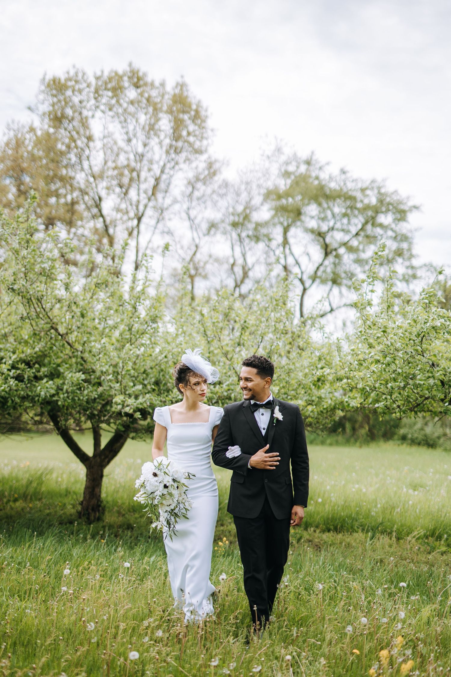 A couple walks through a spring meadow during their wedding photoshoot.