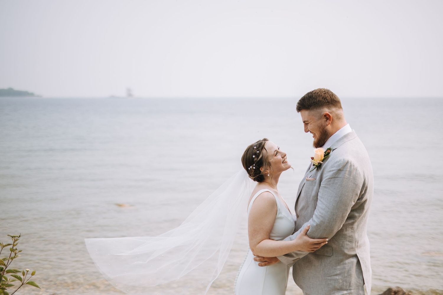 A couple shares a tender moment by the waterfront on their wedding day.