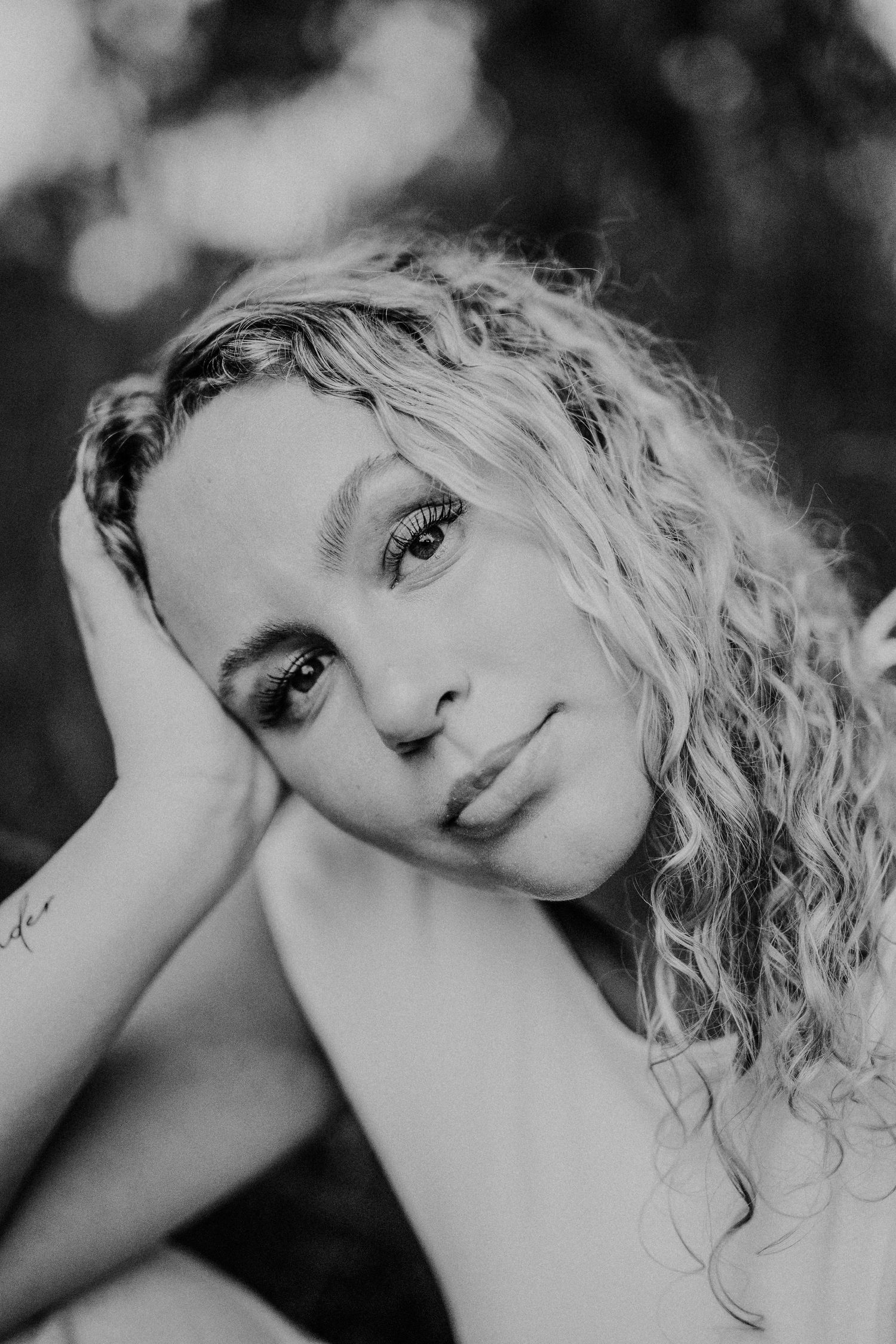 Black and white portrait photograph showing curly blonde hair and soft expression in an artistic headshot.