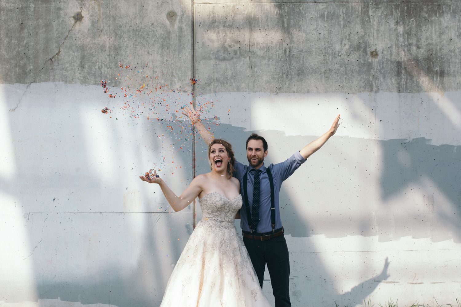 Couple posing playfully against concrete wall with artistic shadows.
