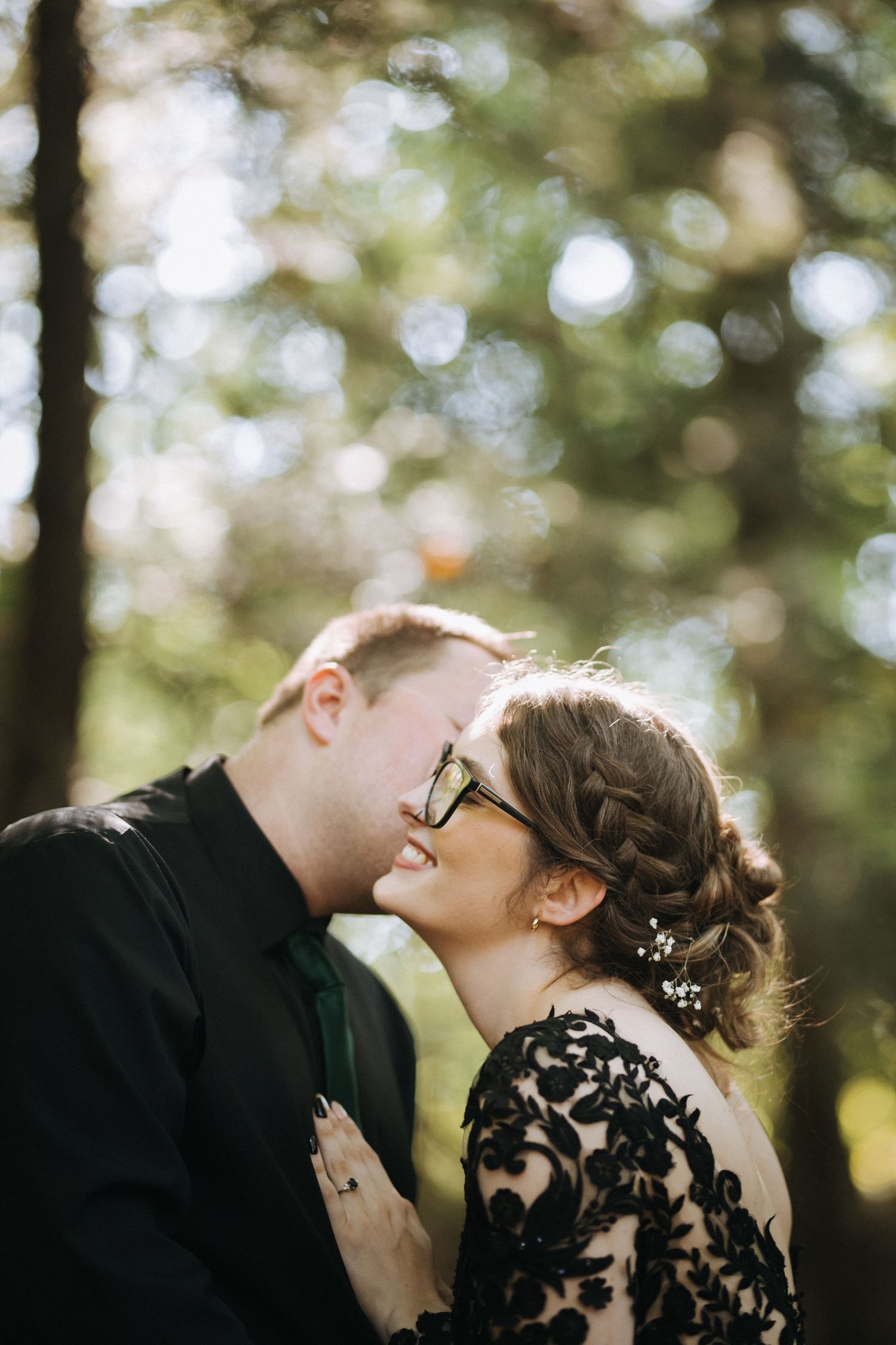 Couple shares intimate moment while surrounded by sunlit trees in outdoor setting.