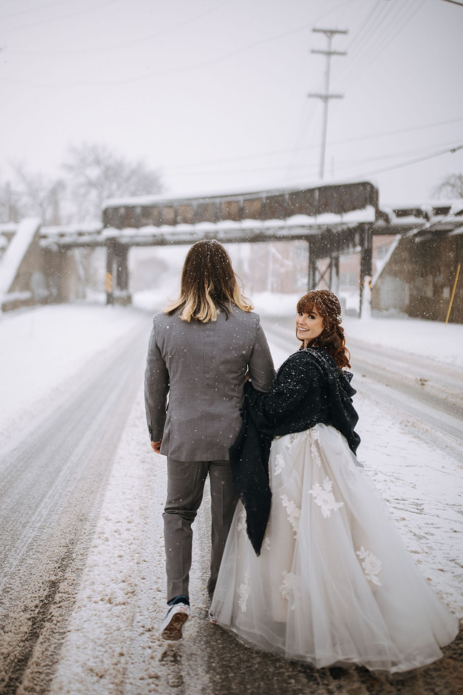 Couple walking together on a snowy road with utility poles and winter landscape.