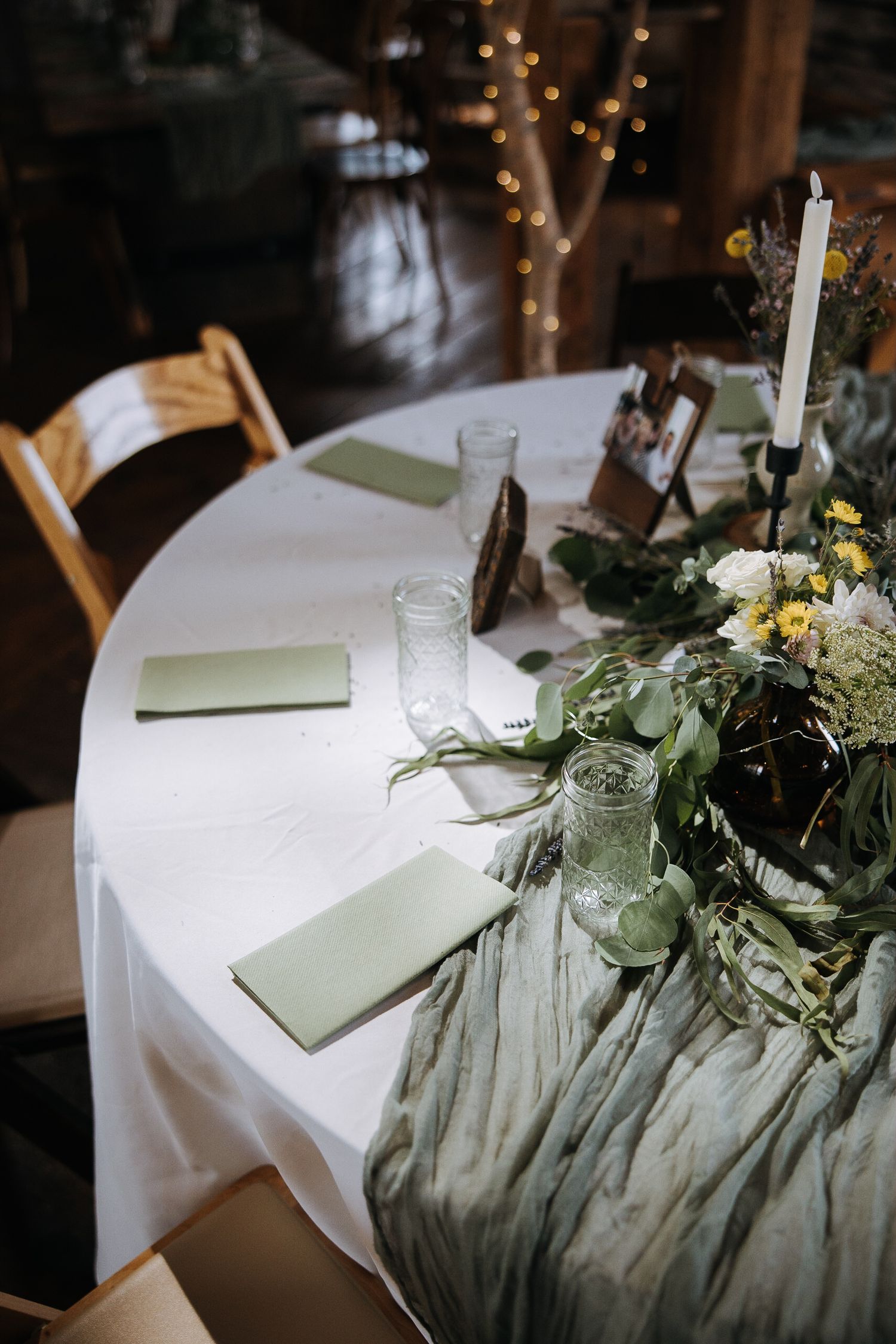 Wedding reception table decor featuring white tablecloths, greenery, and candlesticks.