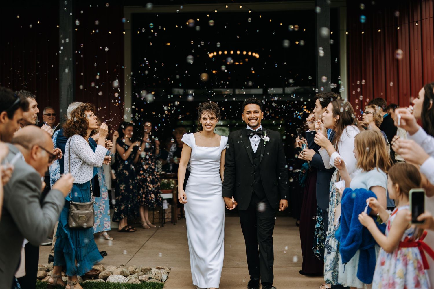 Wedding party celebrates with joyful dancing at an outdoor reception under twinkling lights.