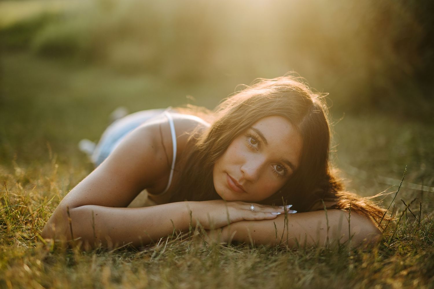 Artistic portrait of someone laying in grass during sunset with warm golden lighting.