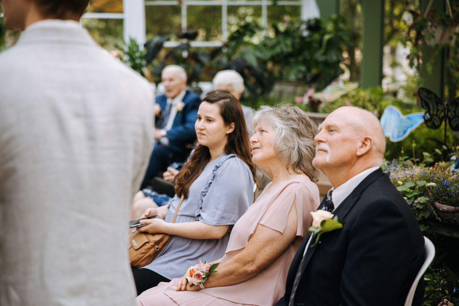 Wedding guests watching ceremony in an outdoor greenhouse space.