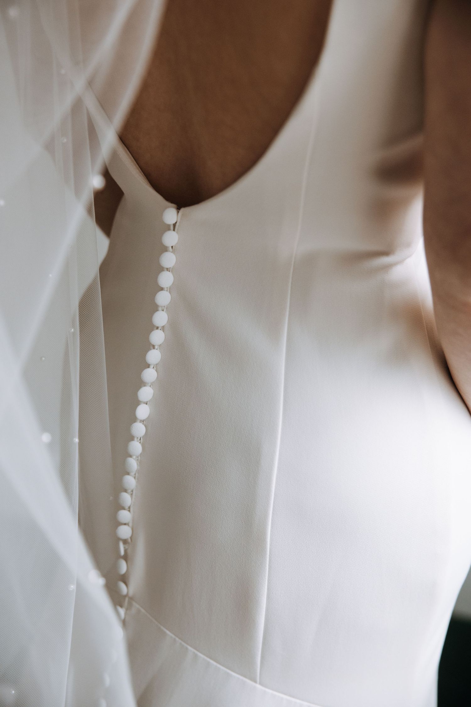 Detail shot of delicate pearl buttons running down the back of a white wedding gown.