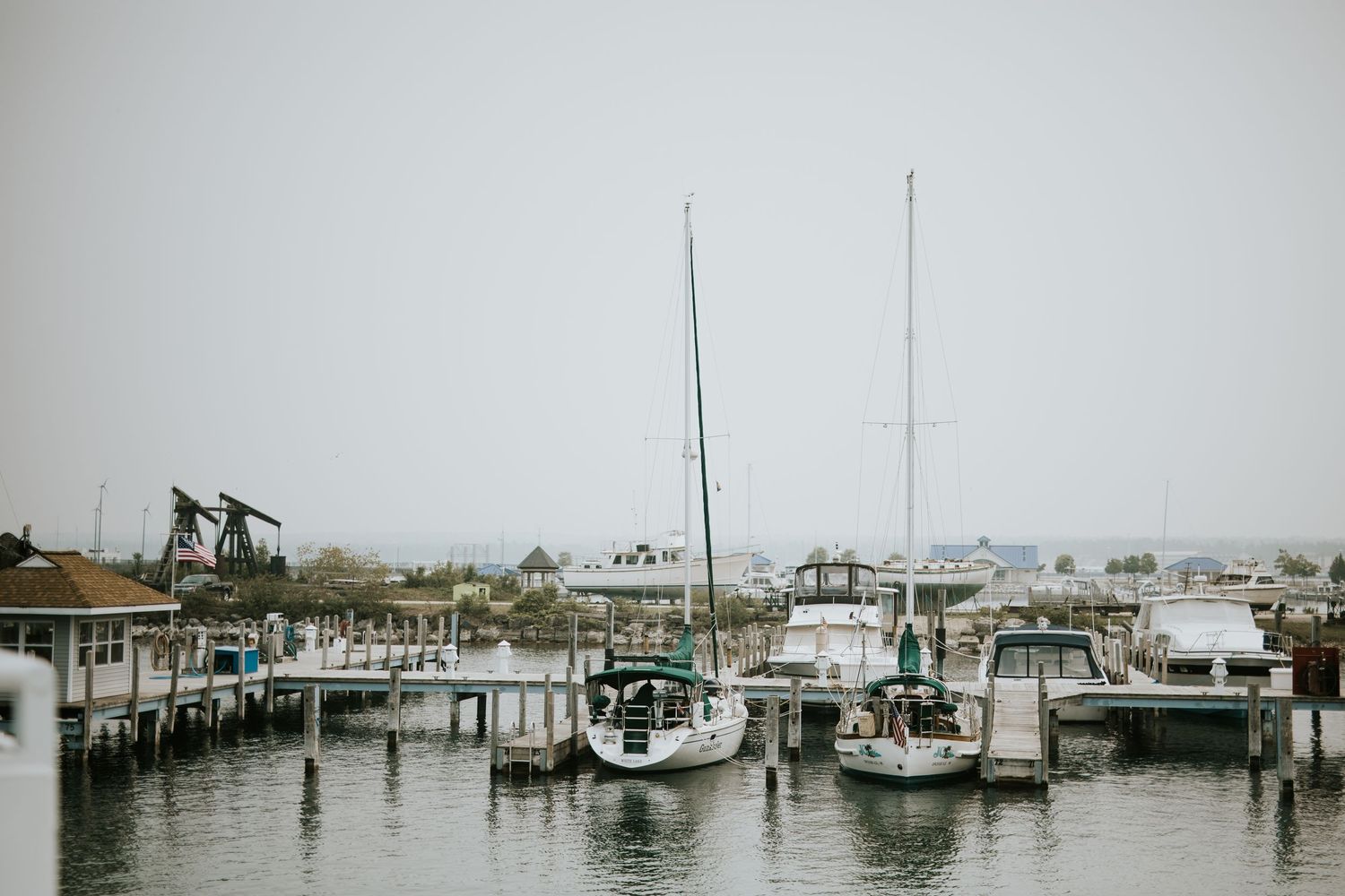 Boats docked at a marina on an overcast day with coastal buildings in the background.