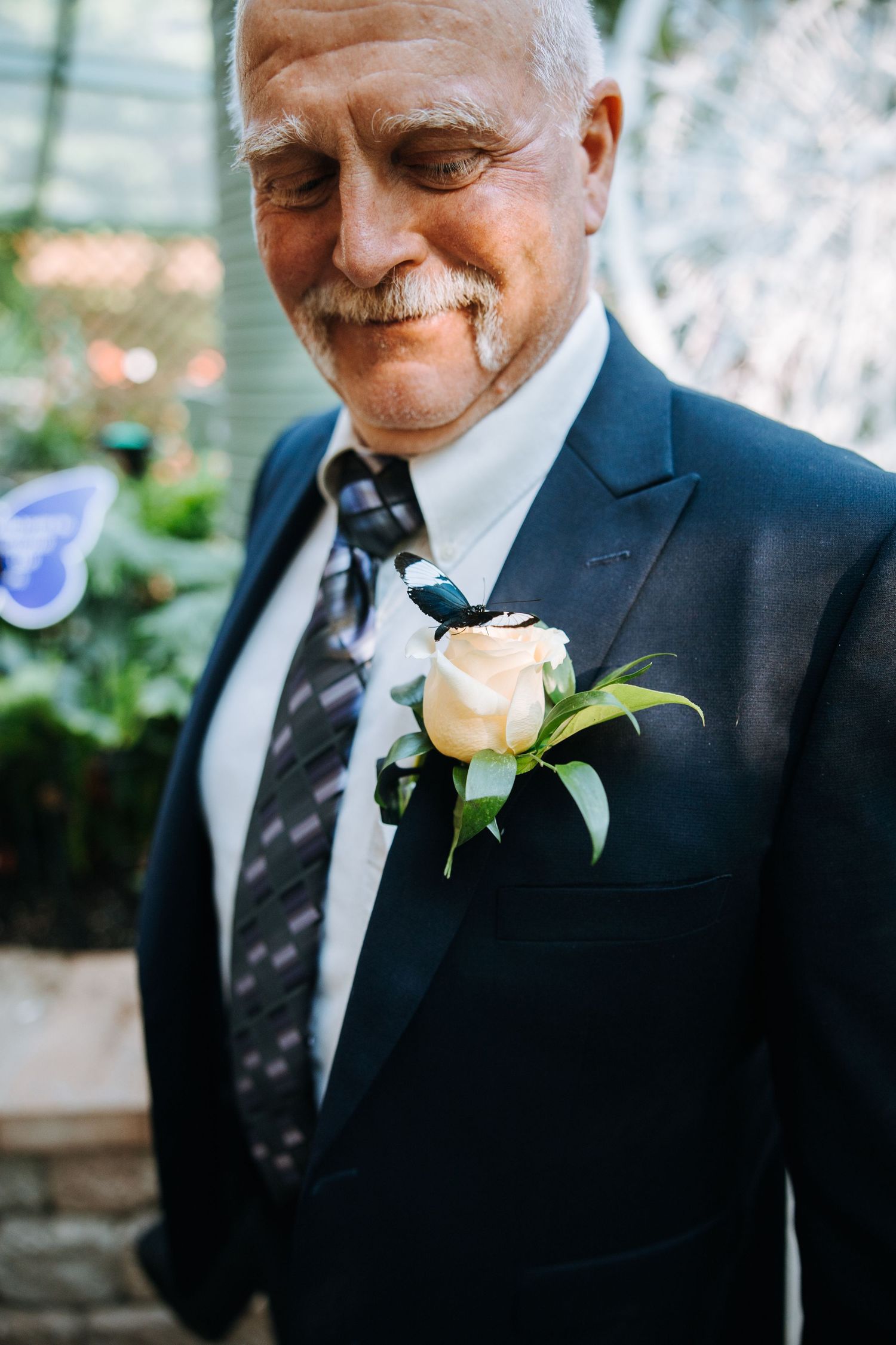 A gentleman in a navy suit with a white rose boutonniere smiles warmly.