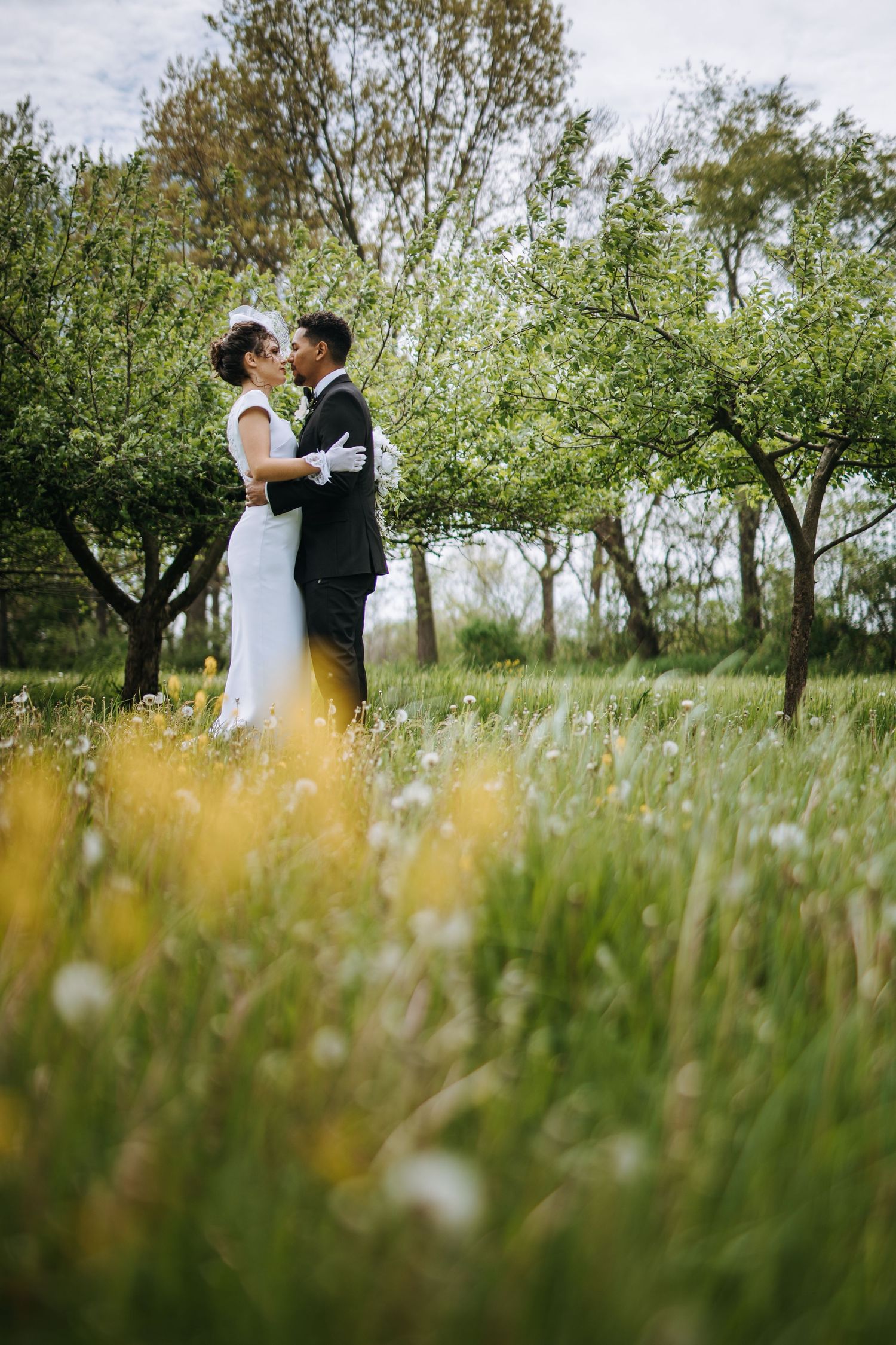 A romantic wedding photoshoot in a meadow with tall grass and trees in the background.