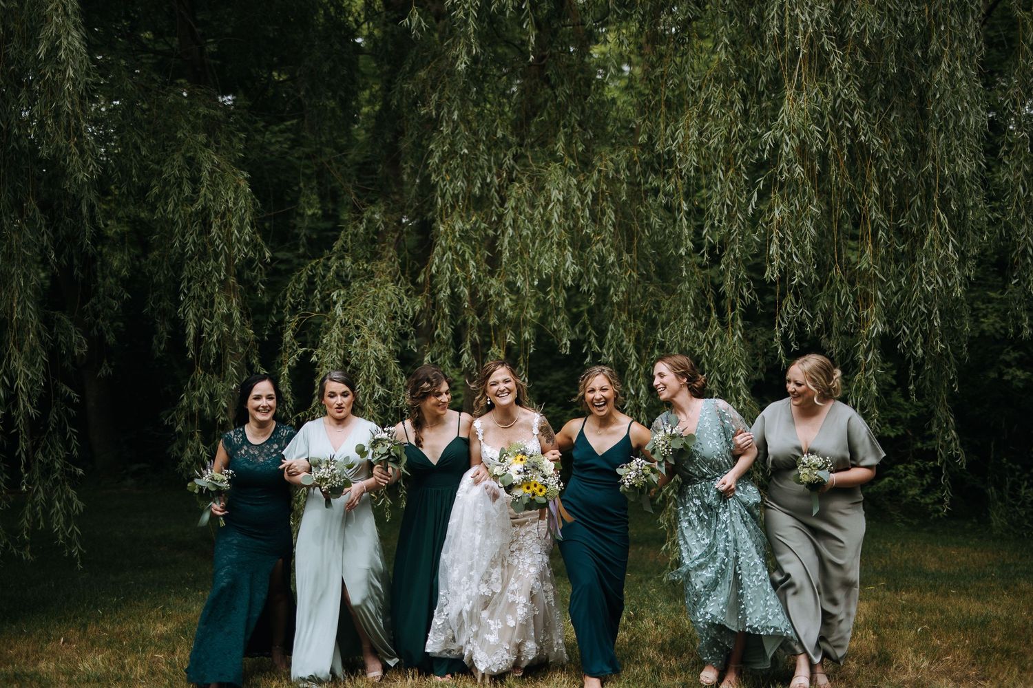 Wedding party celebrating under willow trees during outdoor ceremony.