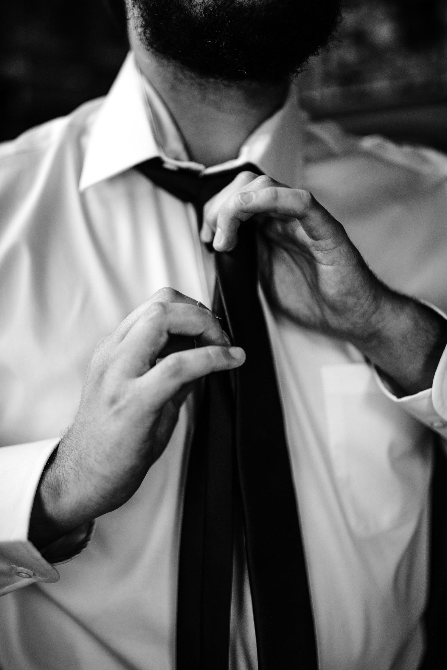 Black and white close-up of hands adjusting tie.