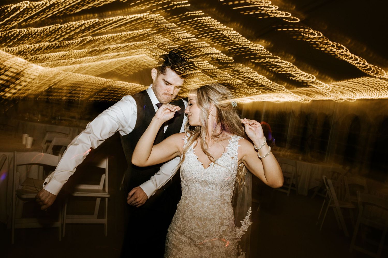 Abstract light trails create golden patterns above wedding reception dance floor.