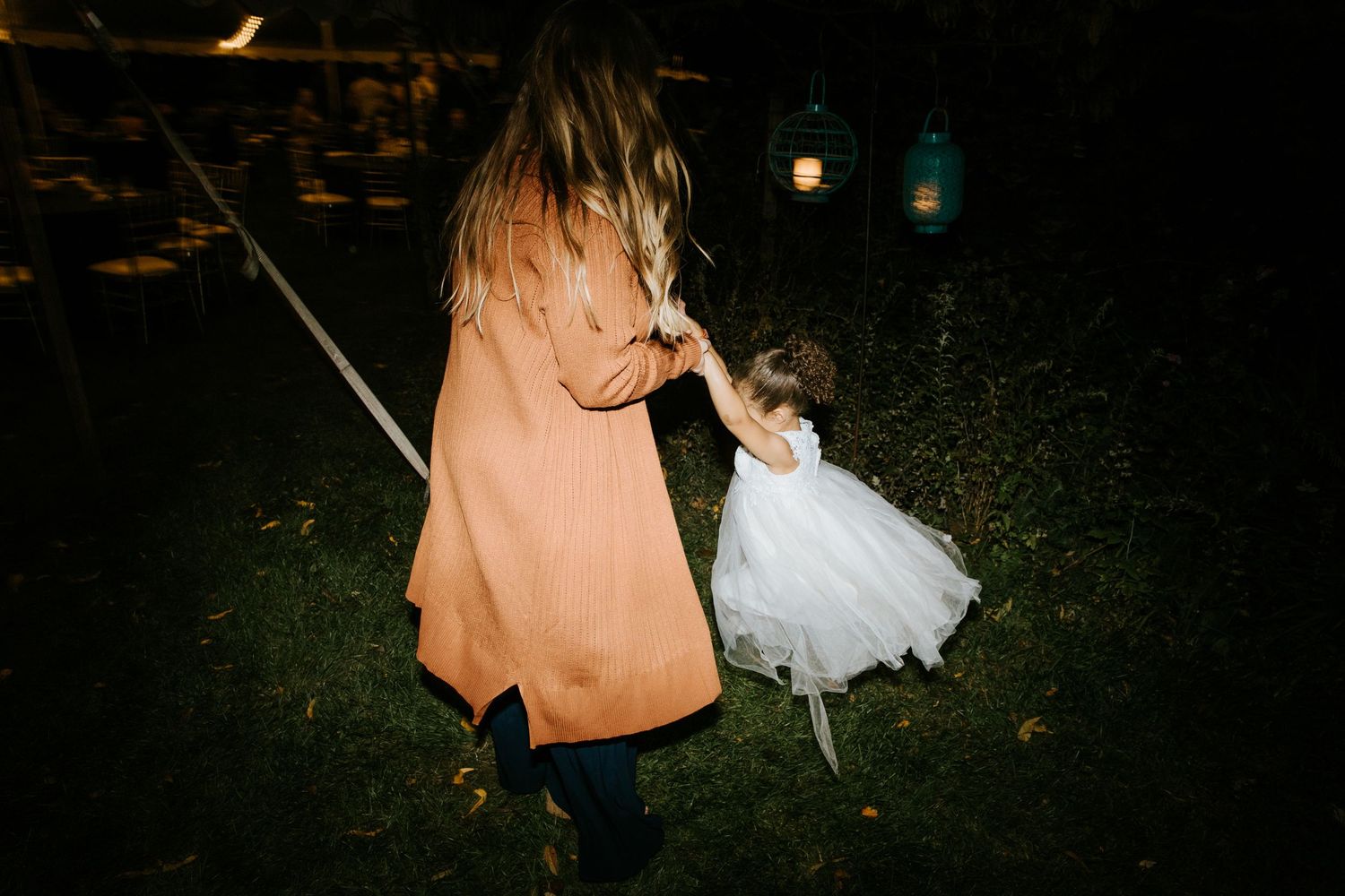 Little girl dances at night under twinkling string lights in an outdoor garden setting.