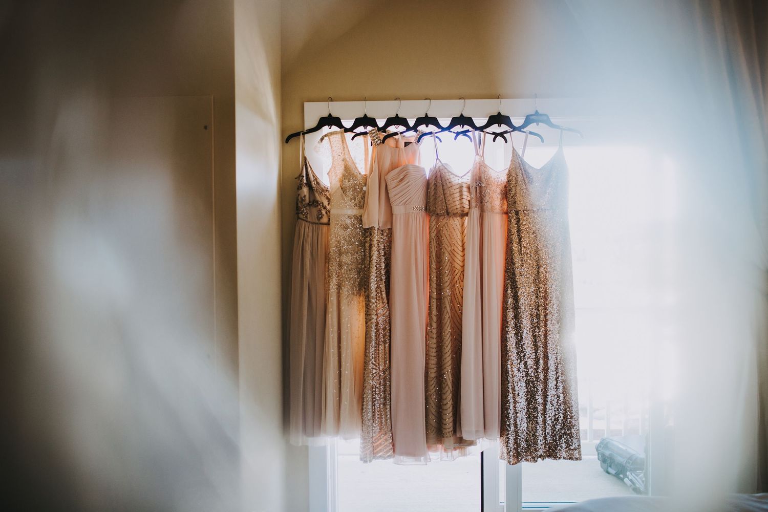 A row of neutral-toned bridesmaid dresses hanging on display in a bridal boutique with soft lighting.
