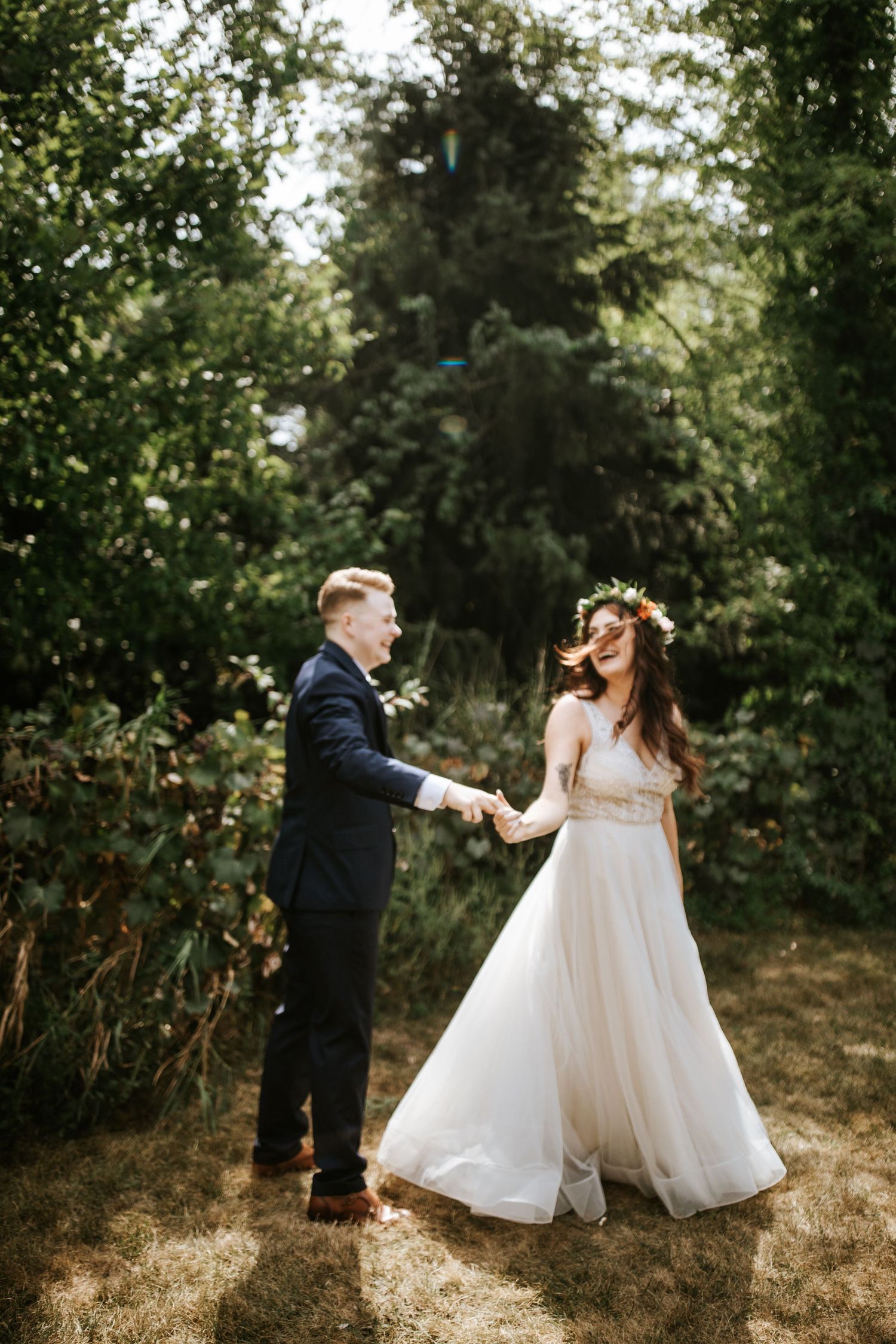 A couple in wedding attire dances and spins joyfully together in a sunlit garden setting.