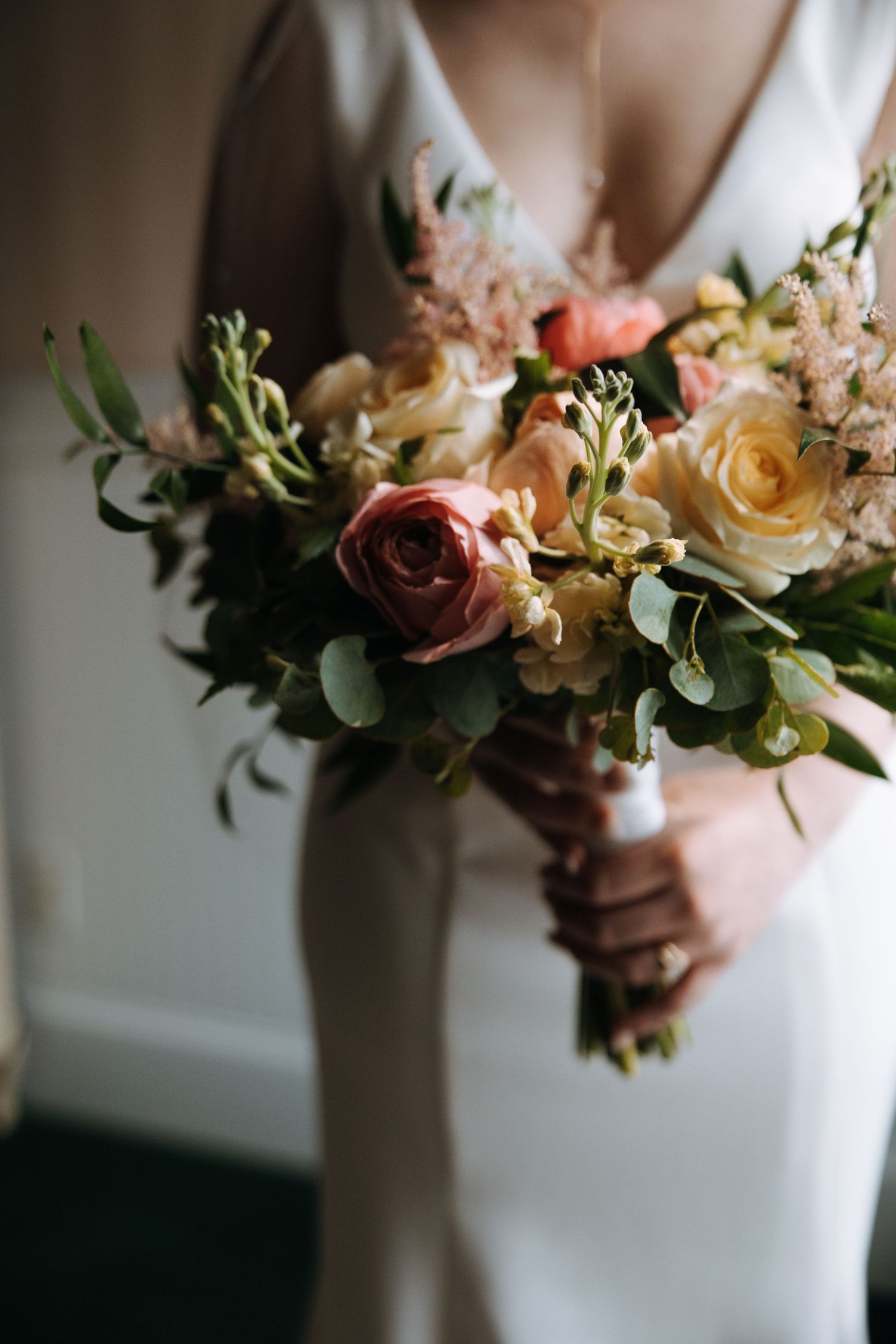 Wedding bouquet featuring peach, yellow and burgundy roses with greenery.